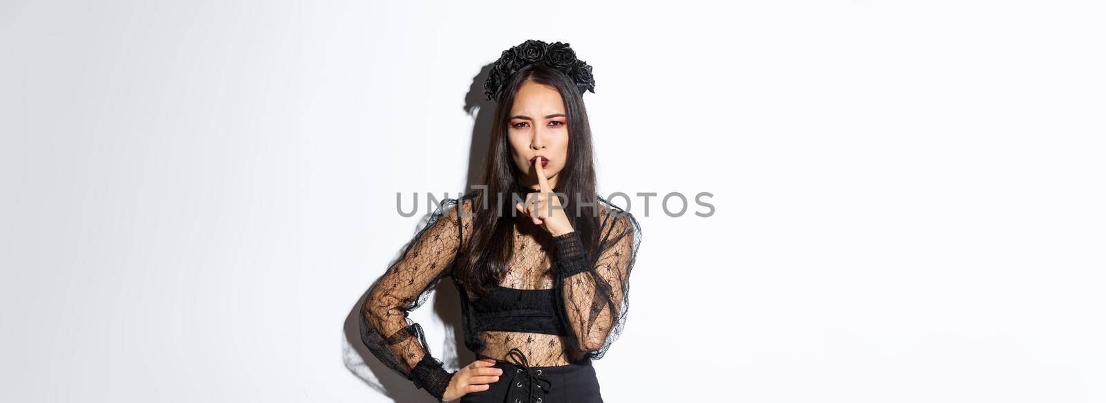 Mysterious asian witch shushing at you with concerned face, hiding secret, tell be quiet. Woman in undead widow costume prepare surprise for halloween, standing over white background by Benzoix