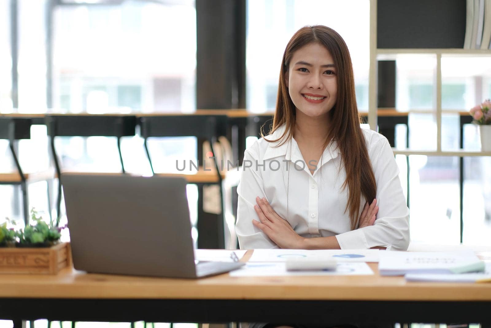 Beautiful smiling Asian businesswoman sitting with arms crossed looking at camera in the office..