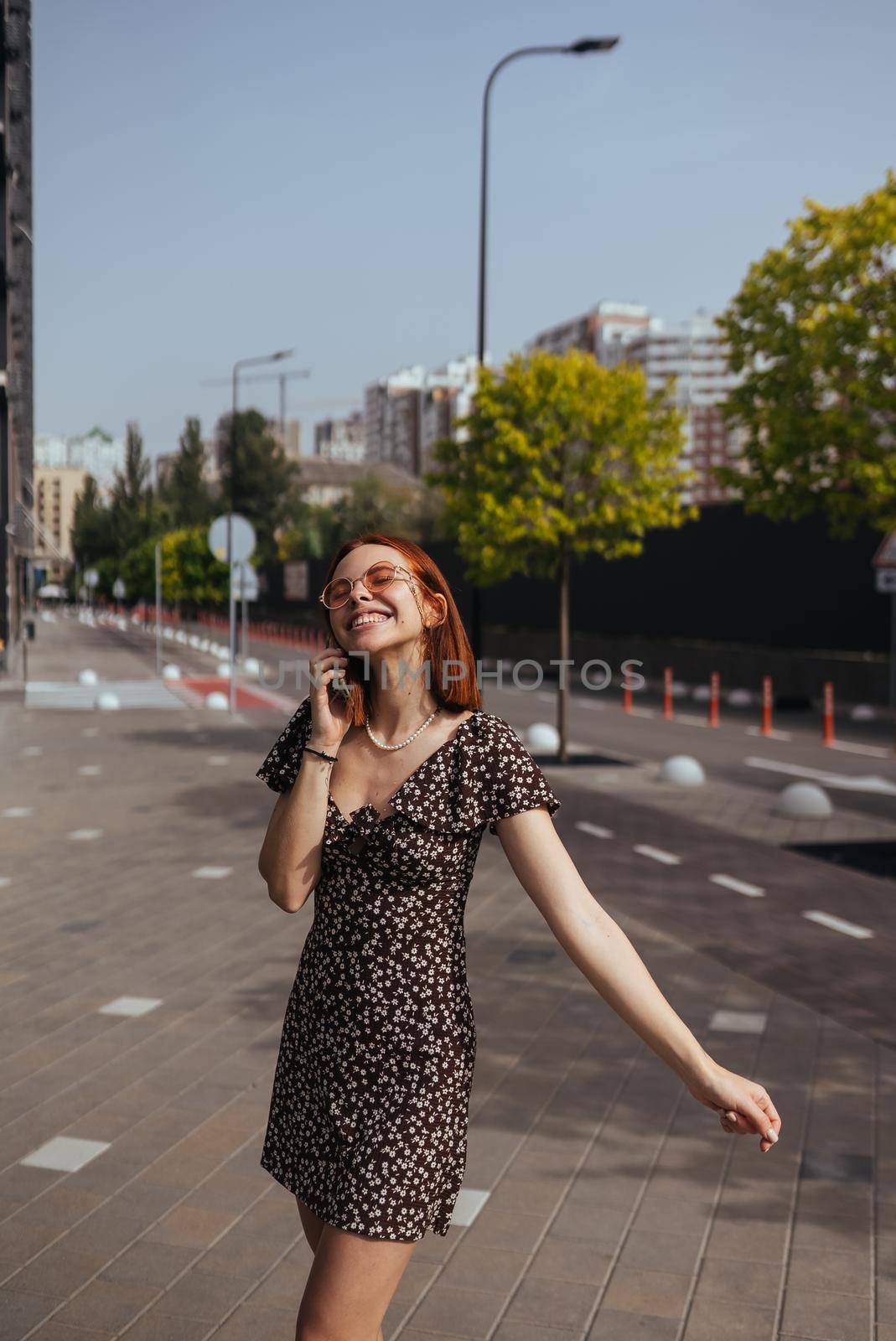 Beautiful woman is walking down the street with smartphone in her hands. Cute girl talking on mobile phone on modern city background
