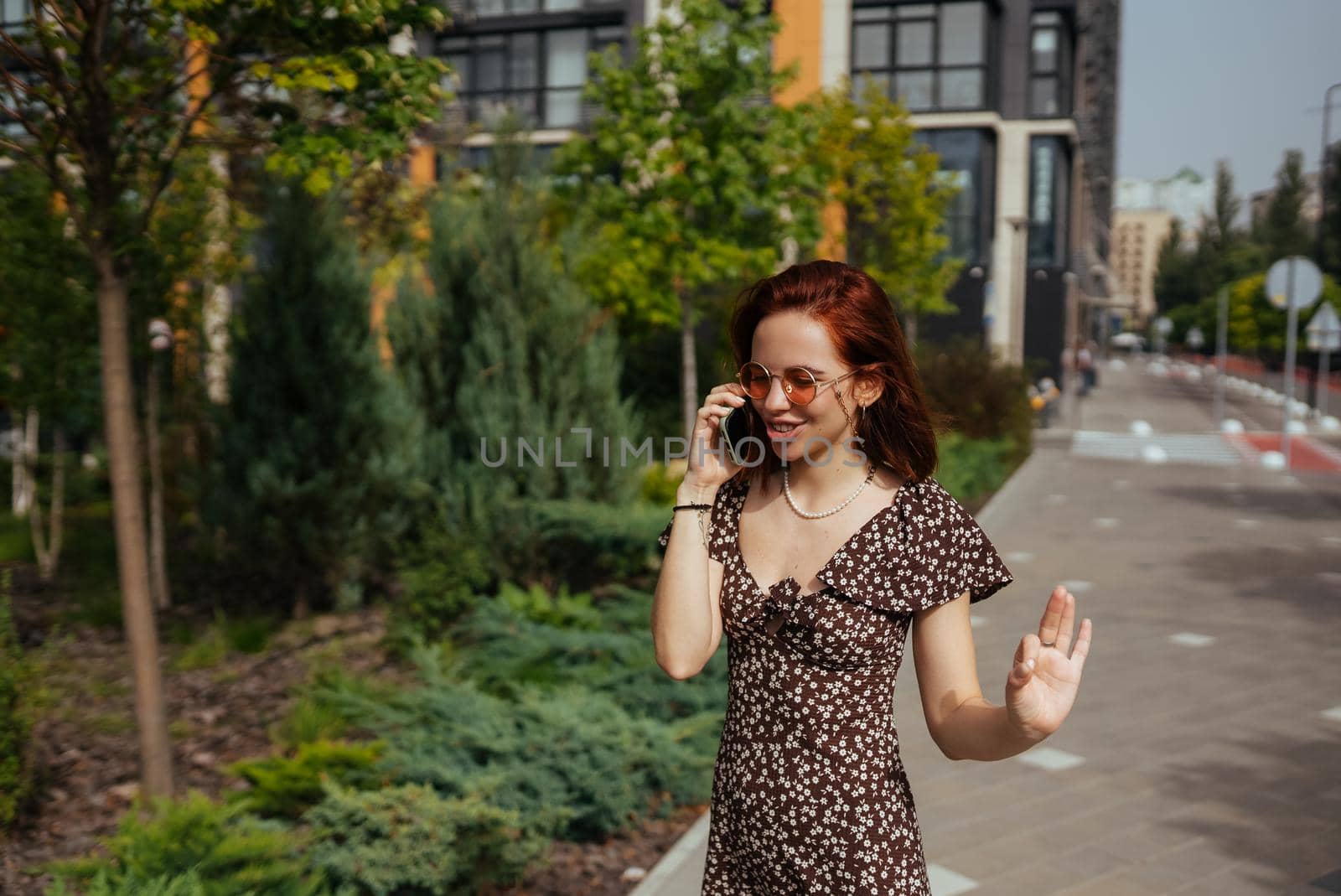 Beautiful woman is walking down the street with smartphone in her hands. Cute girl talking on mobile phone on modern city background