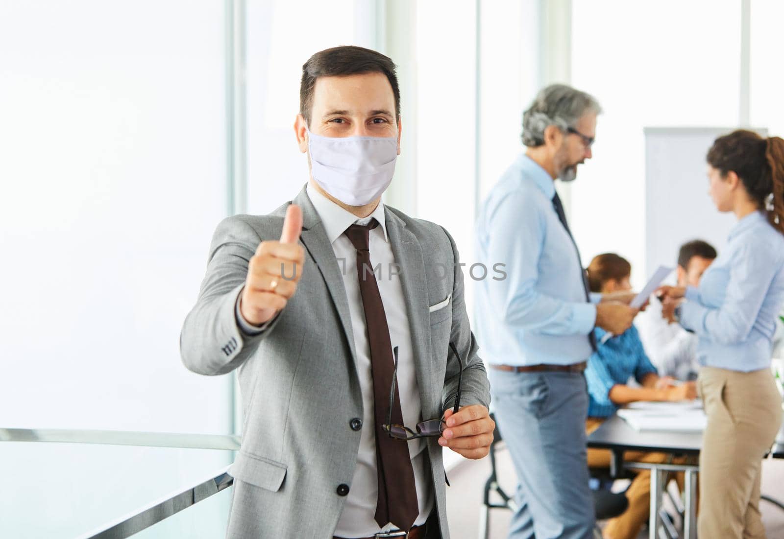 A portrait of a young smiling businessman wearing a ptorective mask during a meeting and presentation in the office. Business concept