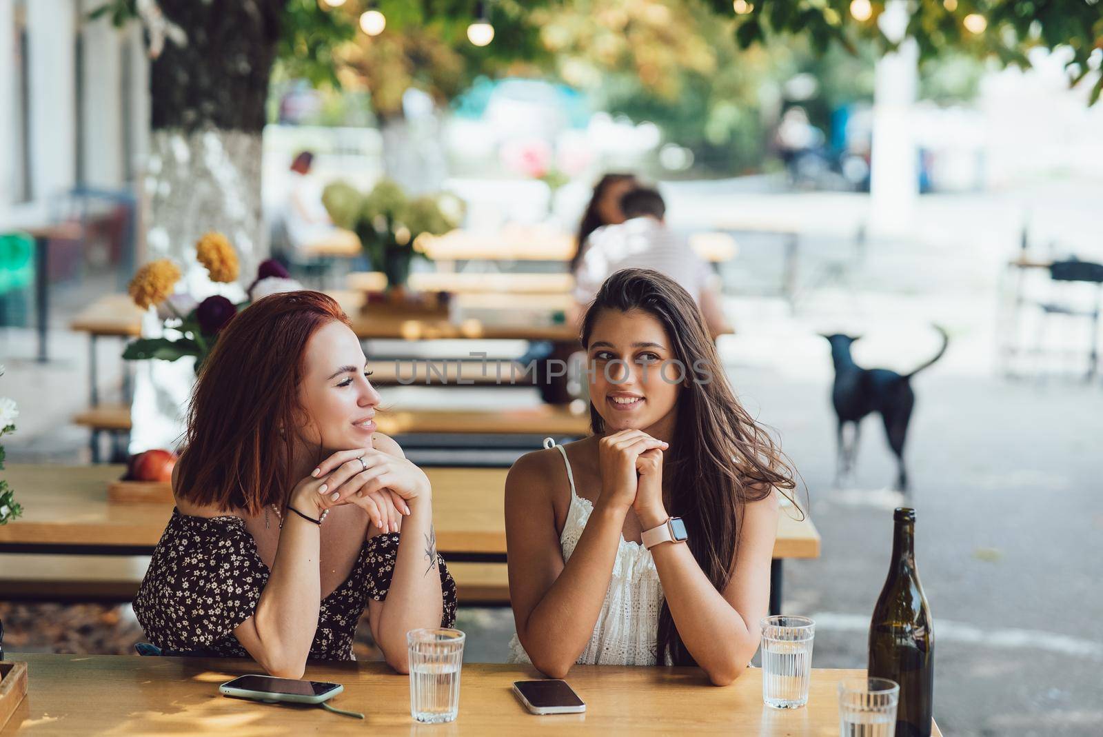 Two young beautiful women girlfriends talking in an outdoor cafe, gossiping, telling news together. Female friendship