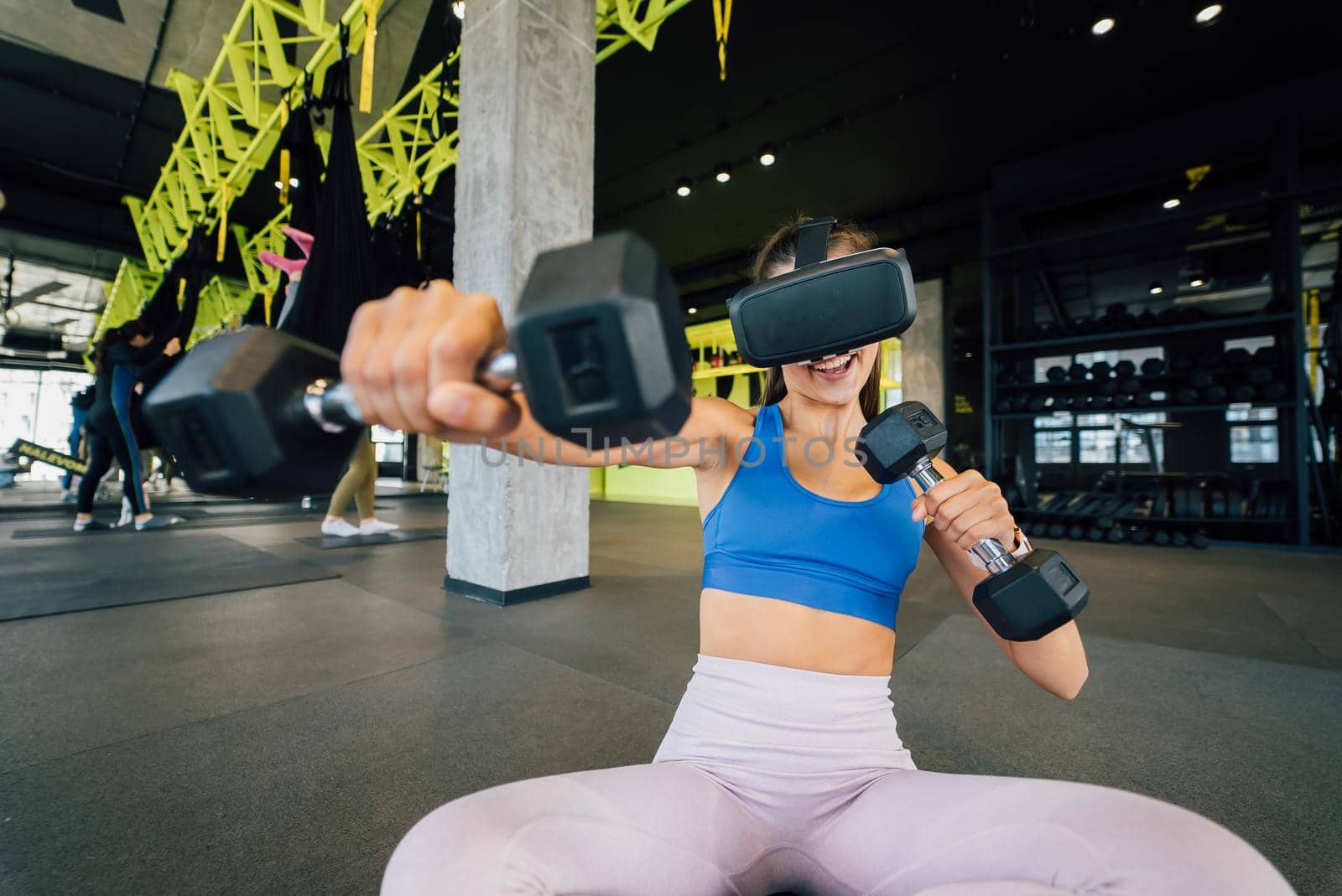 Portrait view of the woman wearing glasses of the virtual reality exercising with dumbbells at gym.