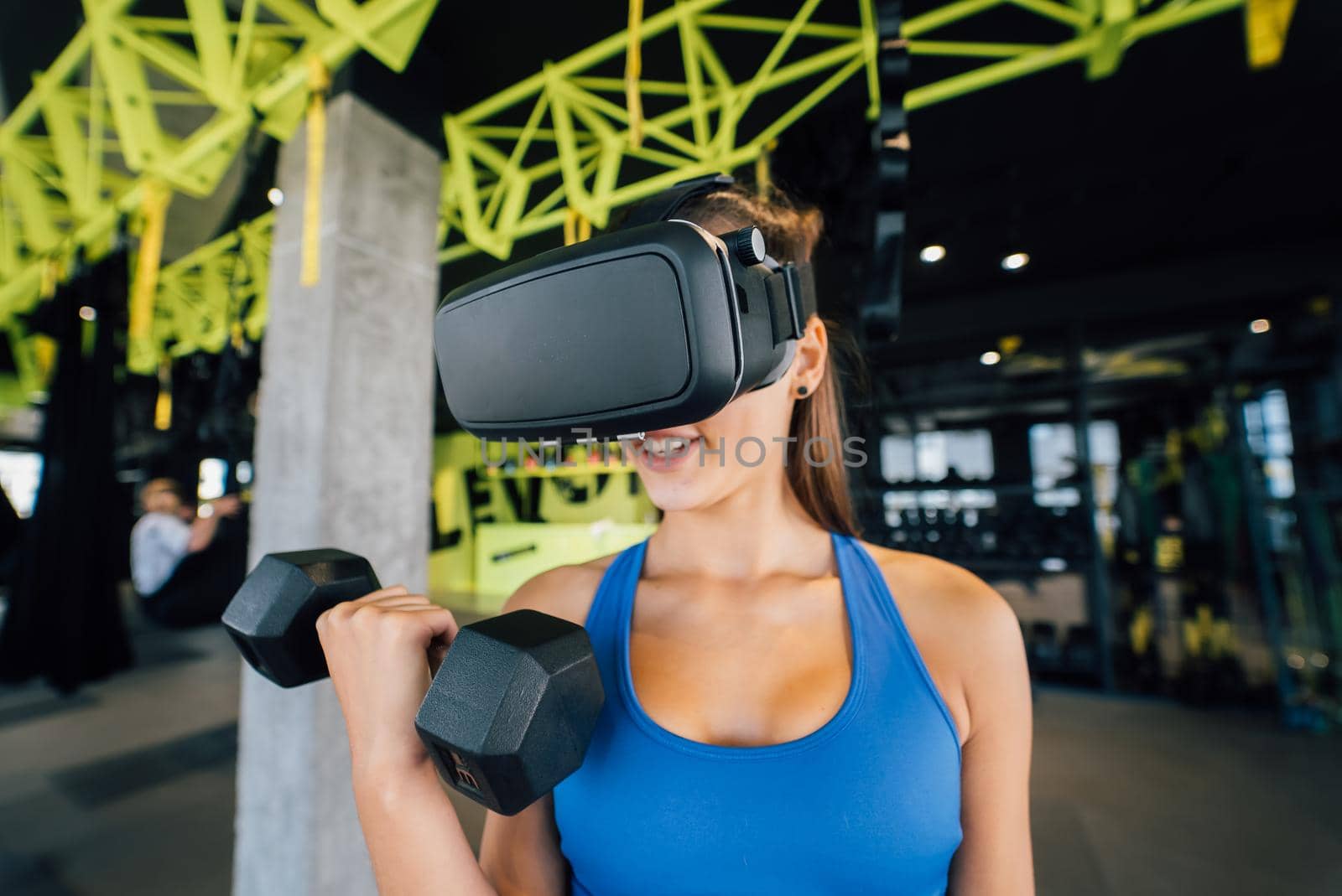 Portrait view of the woman wearing glasses of the virtual reality exercising with dumbbells at gym.
