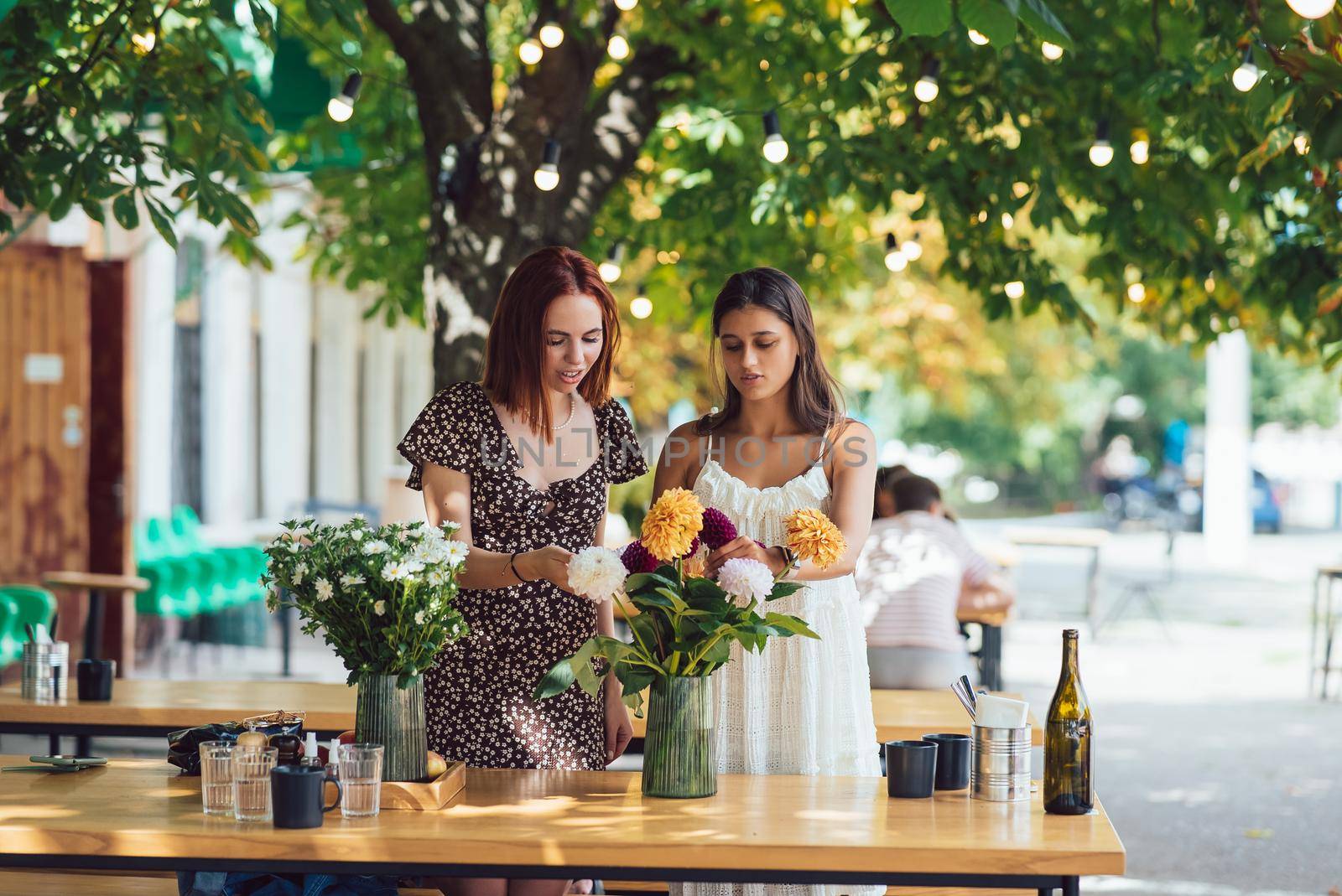 Two young women take orders and make up a beautiful festive bouquet. Floristry and making bouquets at the street caffe. Small business.