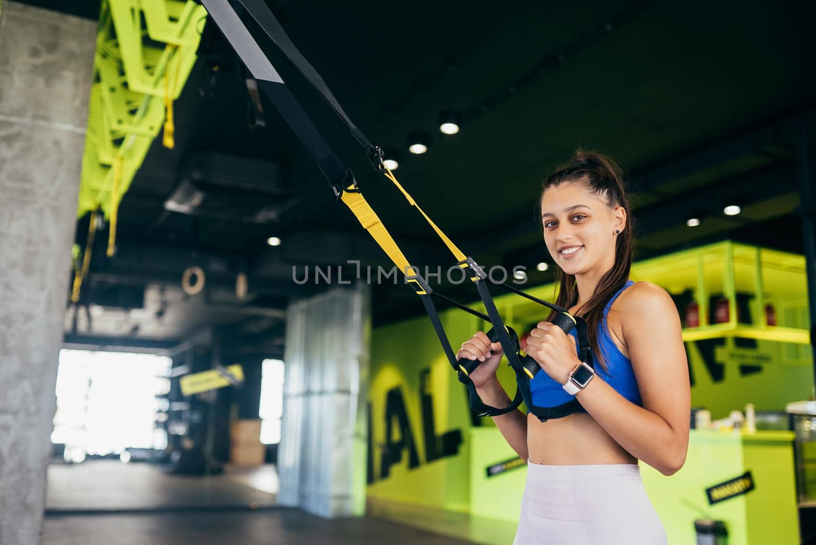 Young athletic woman with perfect body in sportswear doing exercises with trx fitness straps in the gym