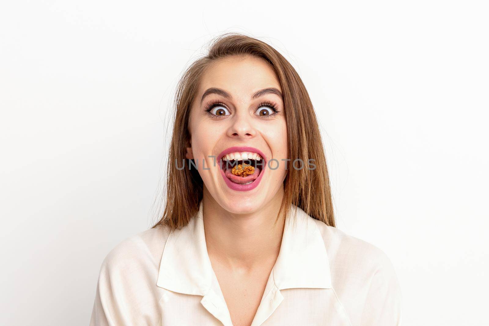 Happy young caucasian woman eating walnuts with an open mouth on white background with copy space. by okskukuruza