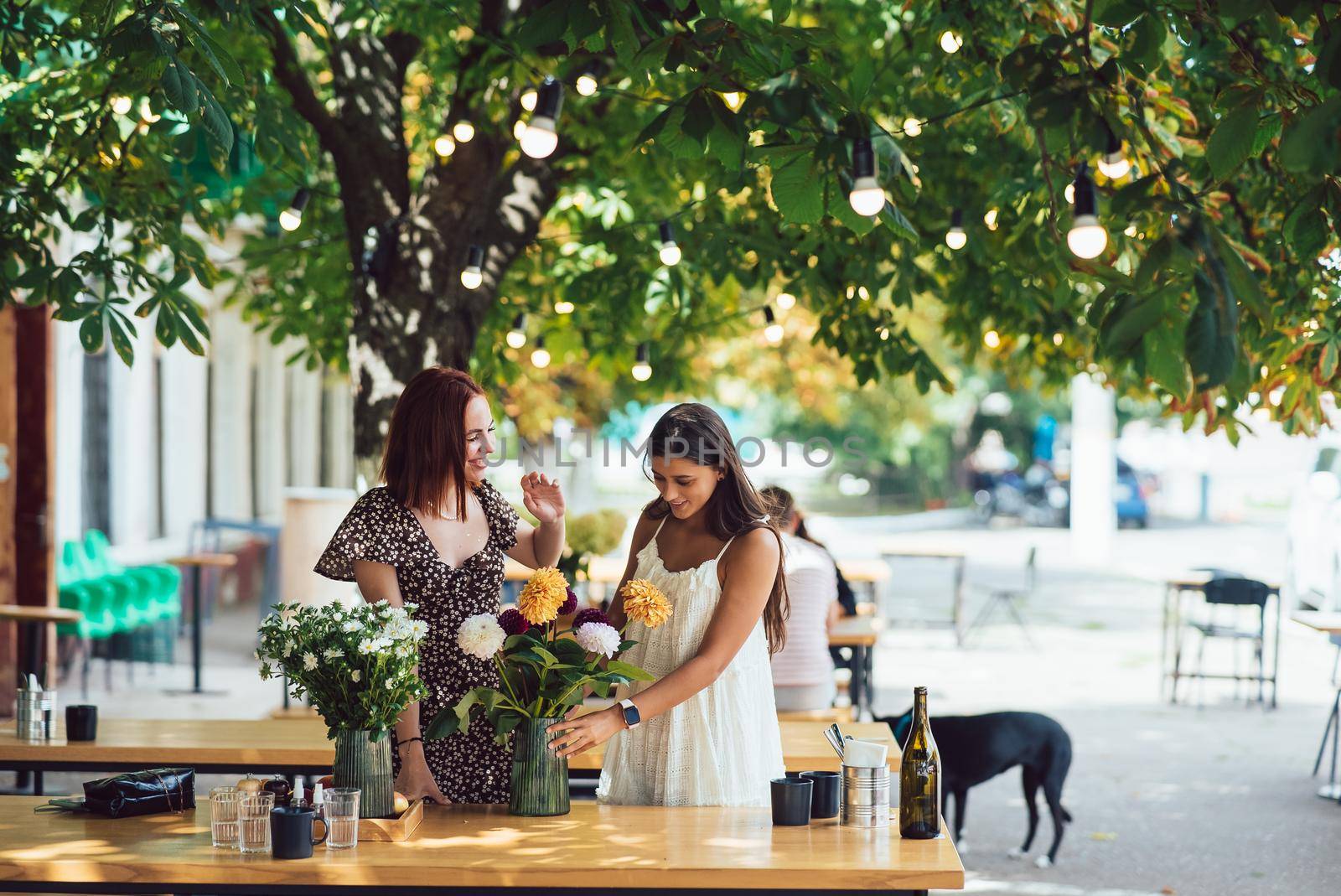 Two young women take orders and make up a beautiful festive bouquet. Floristry and making bouquets at the street caffe. Small business.
