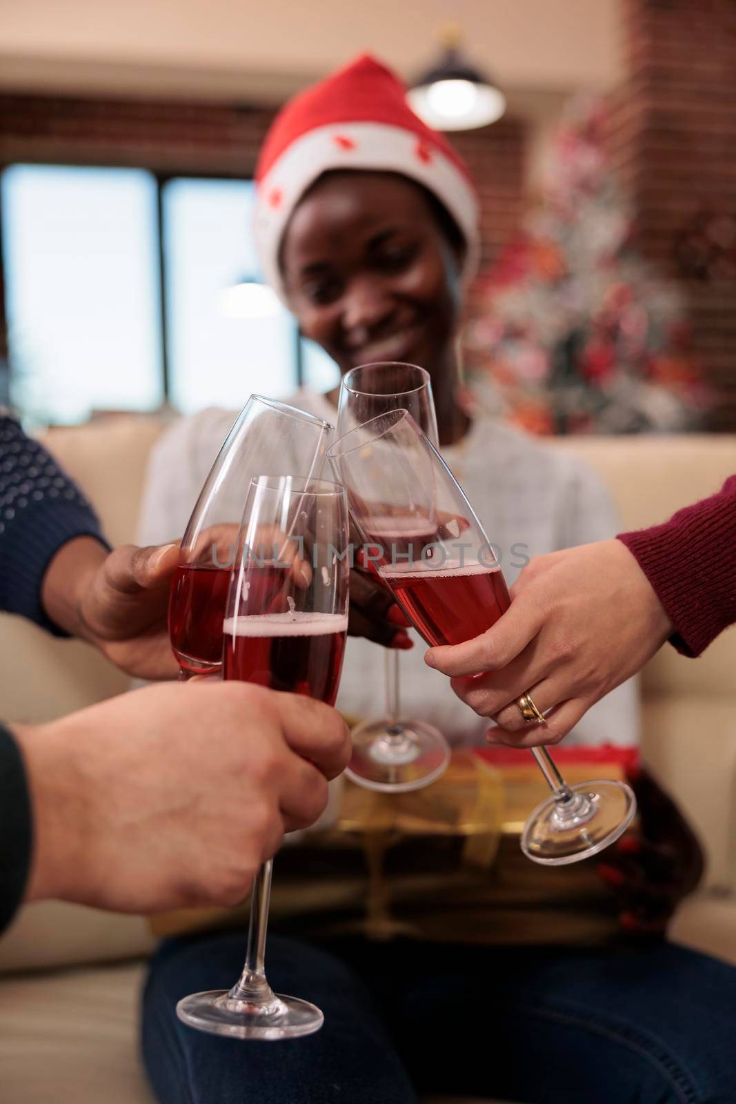 Diverse colleagues clinking glasses of wine at office event, doing cheers sign with alcohol to celebrate christmas eve festivity. Coworkers toasting with alcoholic drink at holiday party. Close up.