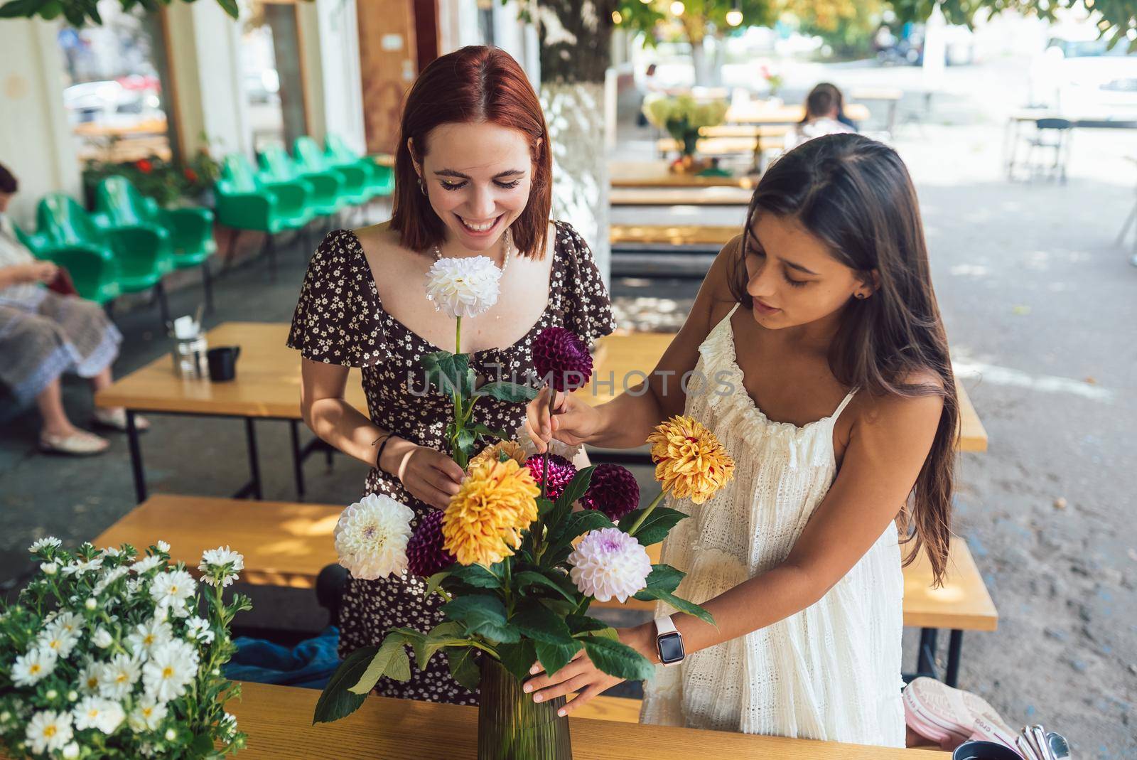 Two young women take orders and make up a beautiful festive bouquet. Floristry and making bouquets at the street caffe. Small business.