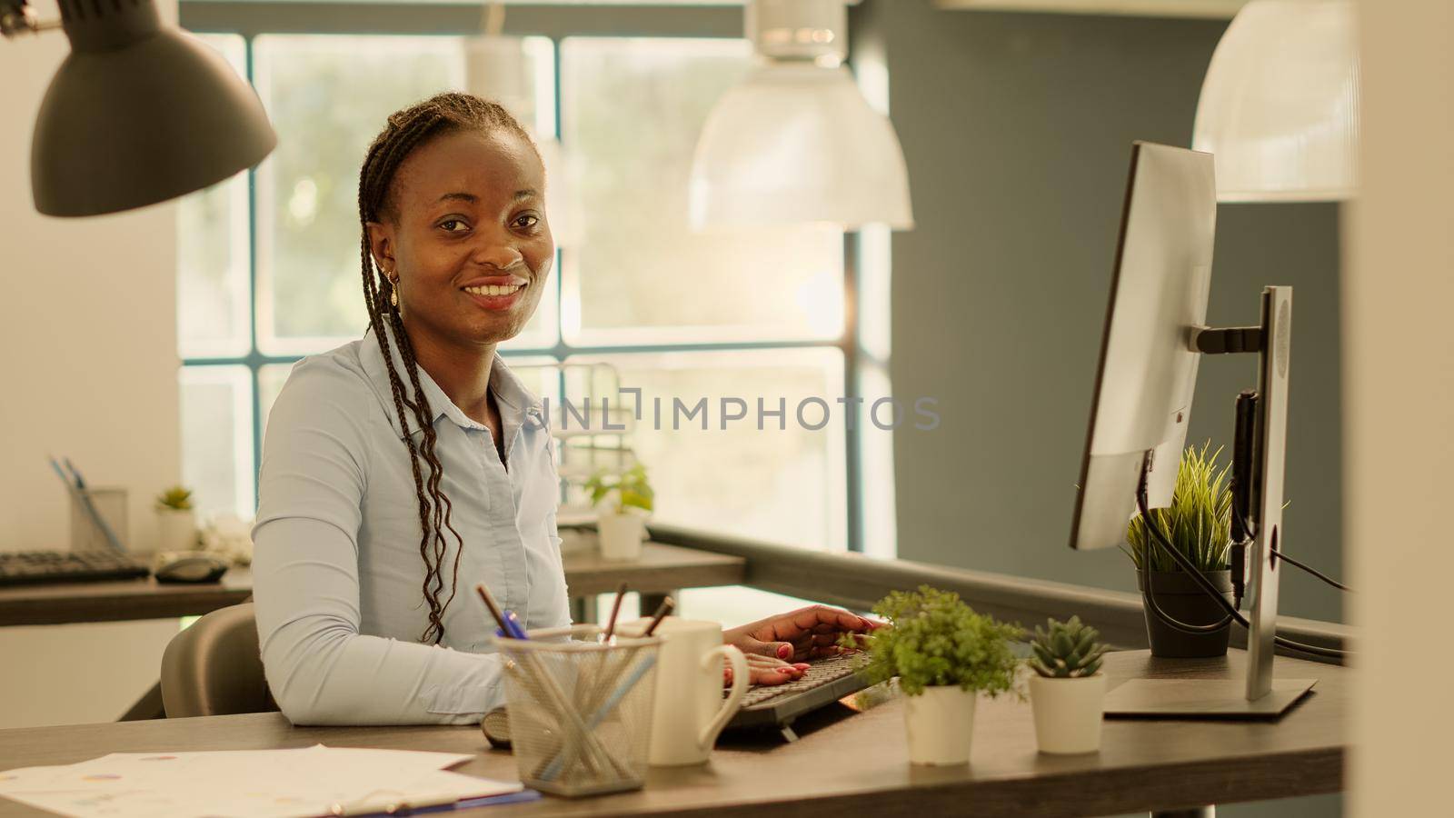 Portrait of african american woman planning business report on computer with company network. Working with research information charts on monitor to create presentation and send email.