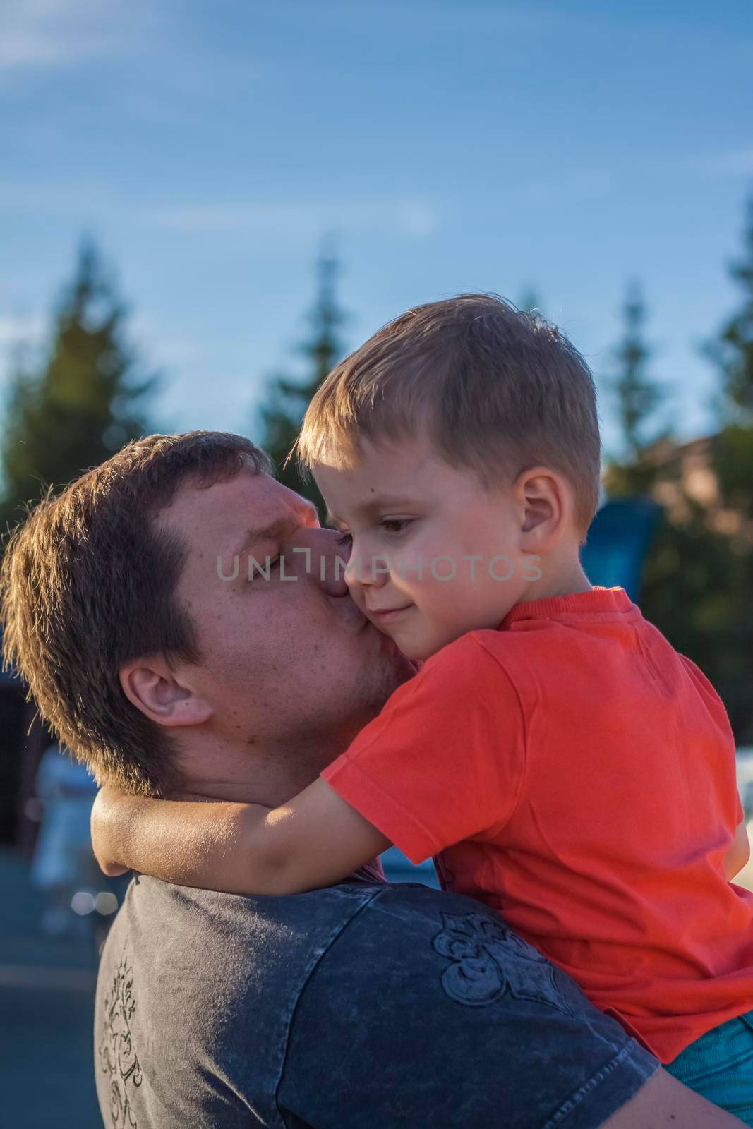 The father hugs and kisses his son on the cheek, whom he holds in his arms. Father and son. Family