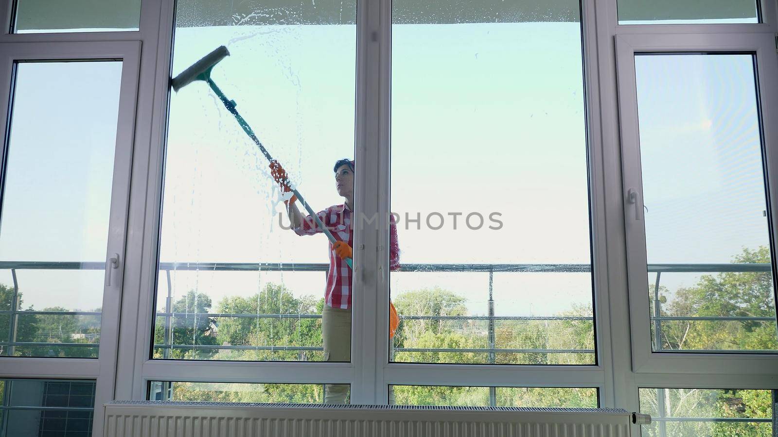 smiling Caucasian Beautiful woman, housewife or Cheerful female worker of cleaning service, in gloves, Cleaning, washing Windows by special mop, enjoying her work. Cleaning lady. High quality photo
