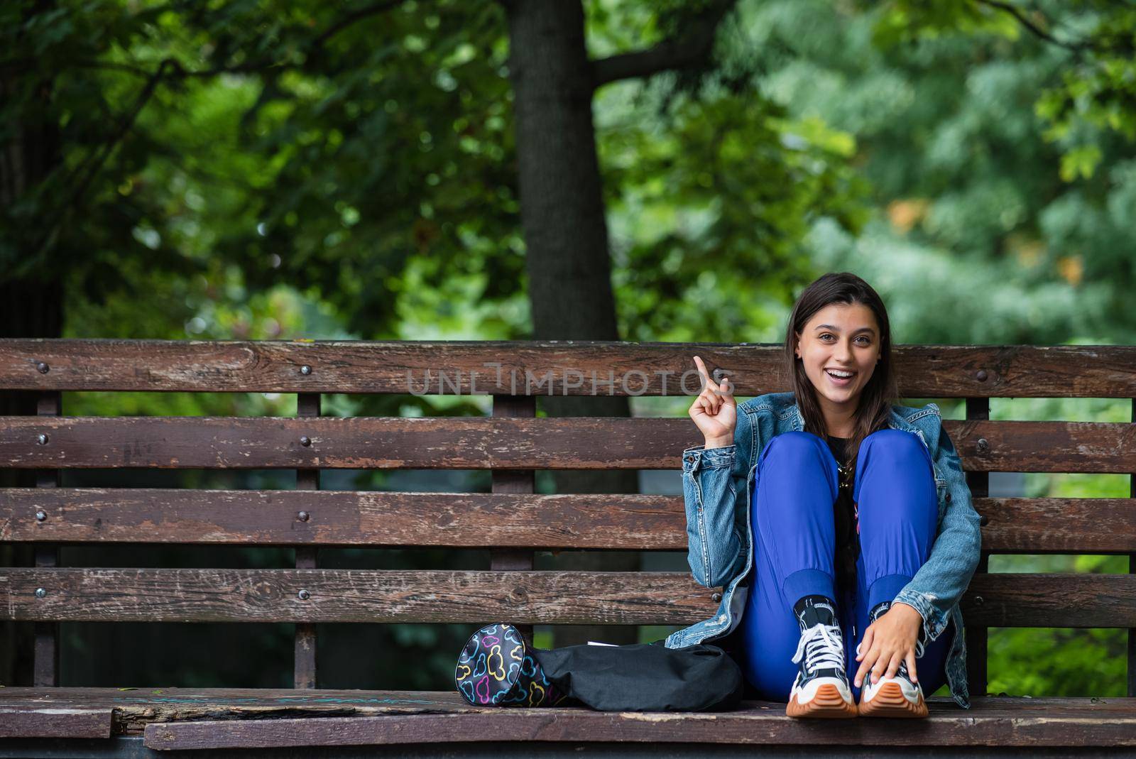 Model pointing fingers at an empty space next to her, the park is out of focus in the background
