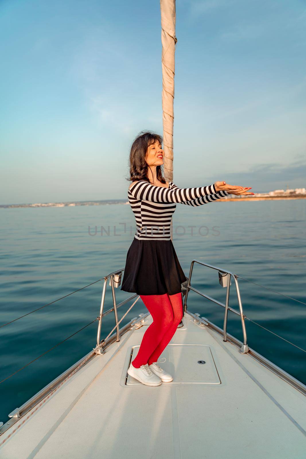 Woman standing on the nose of the yacht at a sunny summer day, breeze developing hair, beautiful sea on background by Matiunina