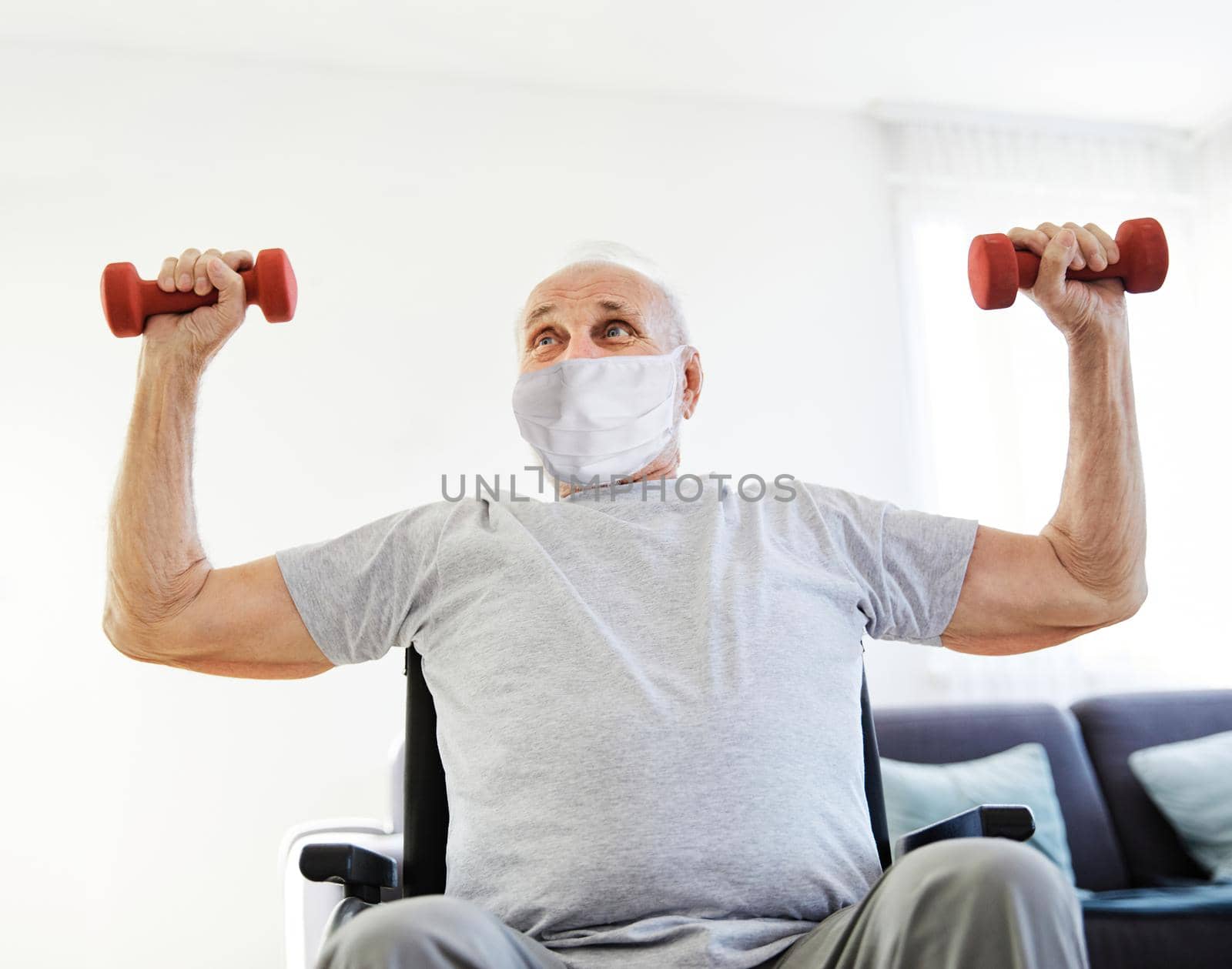 Happy senior man in wheelchair wearing protective mask exercising at home or nursing home