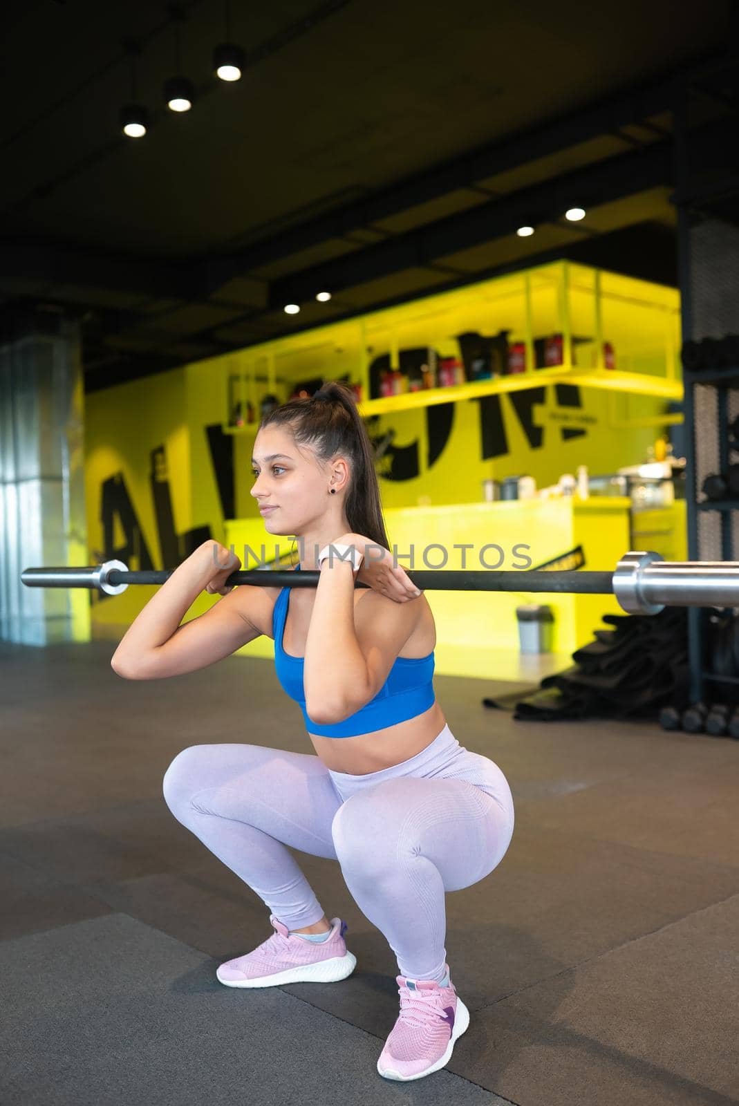 Beautiful and strong young woman doing sit-ups with a barbell for growth of buttocks.