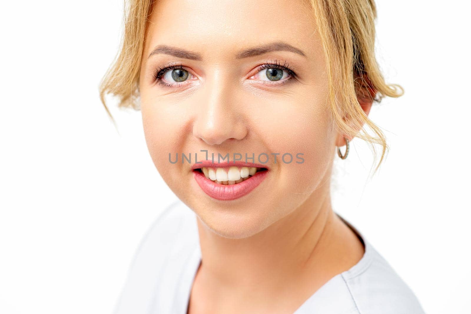 Close-up portrait of young smiling female caucasian healthcare worker standing staring at the camera on white background