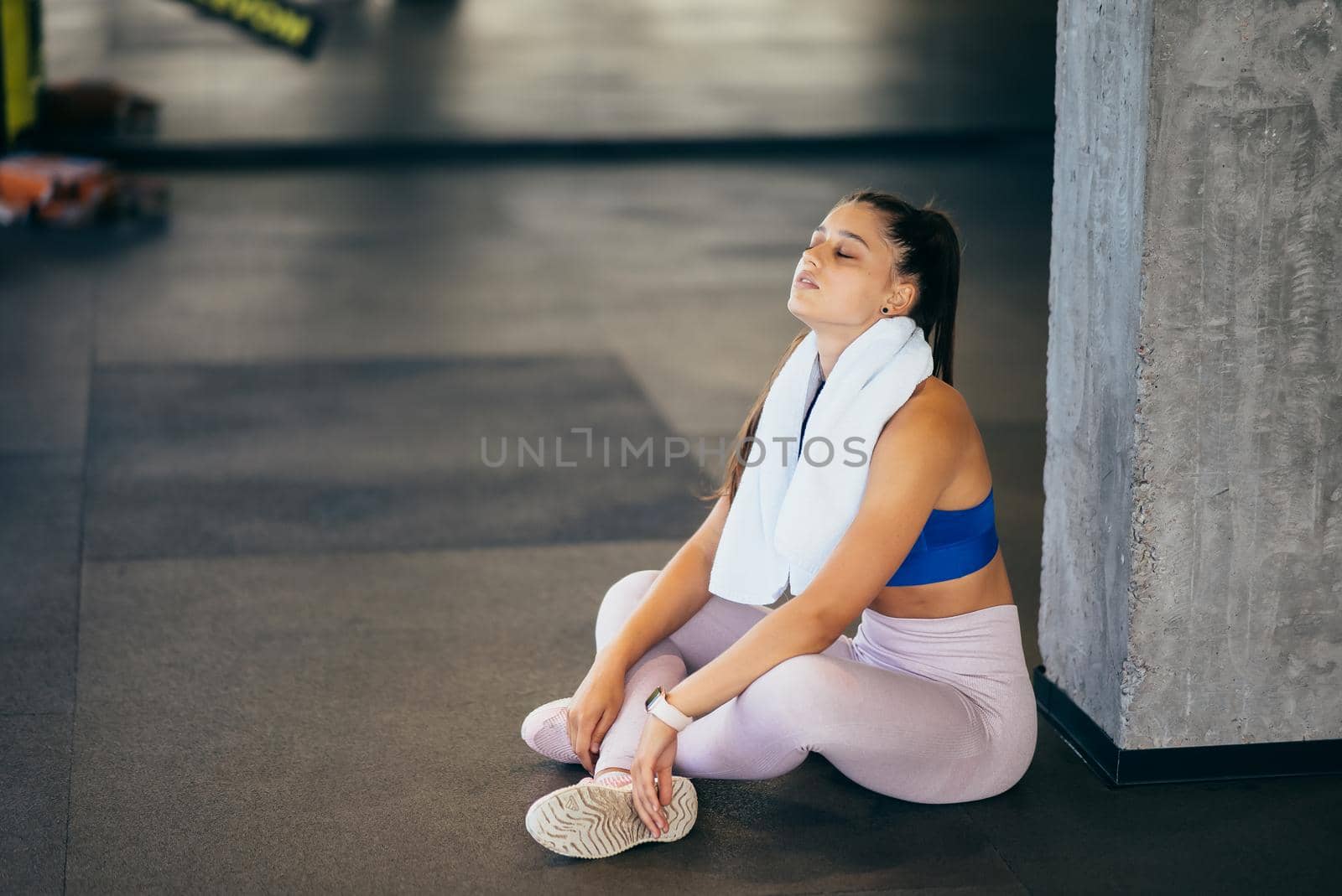 Healthy young female sitting relaxed after training in gym. Woman resting after workout at gym.