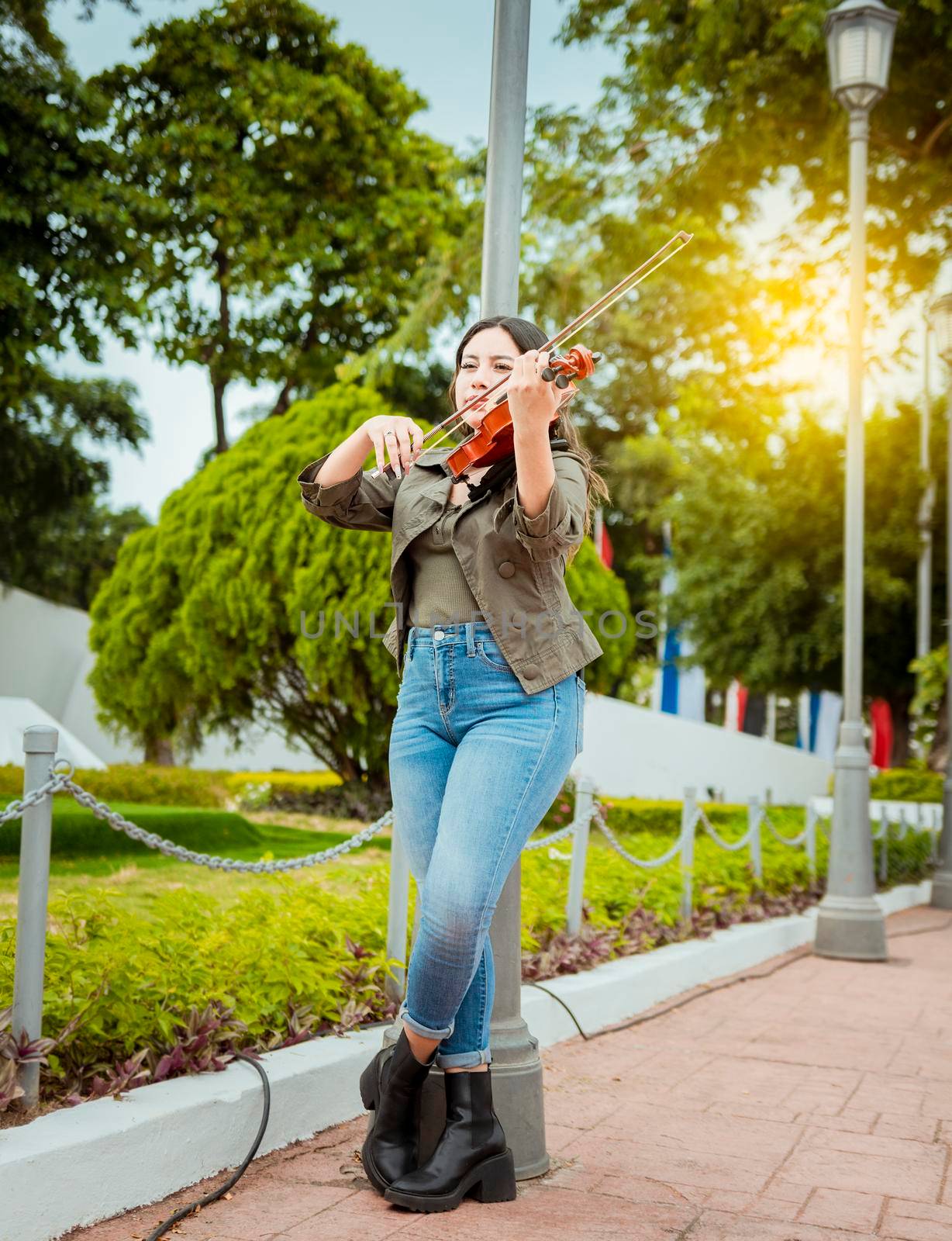 Woman playing violin in the street. Portrait of violinist girl playing in the street. Woman artist playing violin outdoors, Girl lying down playing violin in a park by isaiphoto