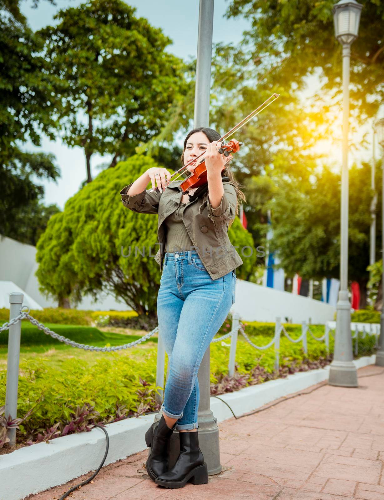 Woman playing violin in the street. Portrait of violinist girl playing in the street. Woman artist playing violin outdoors, Girl lying down playing violin in a park