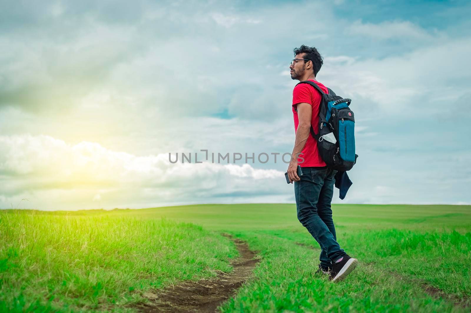 Side view of backpacking man on a beautiful road in the countryside. Young explorer man walking in a green field, Backpacker man walking in a beautiful field.
