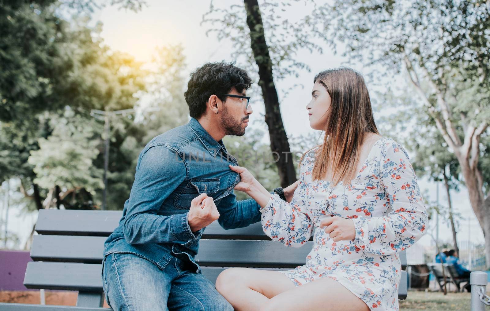 Upset couple arguing on a park bench. Young couple arguing sitting on a park bench, Concept of aggressive couples in the park. Man arguing with his girlfriend sitting in a park