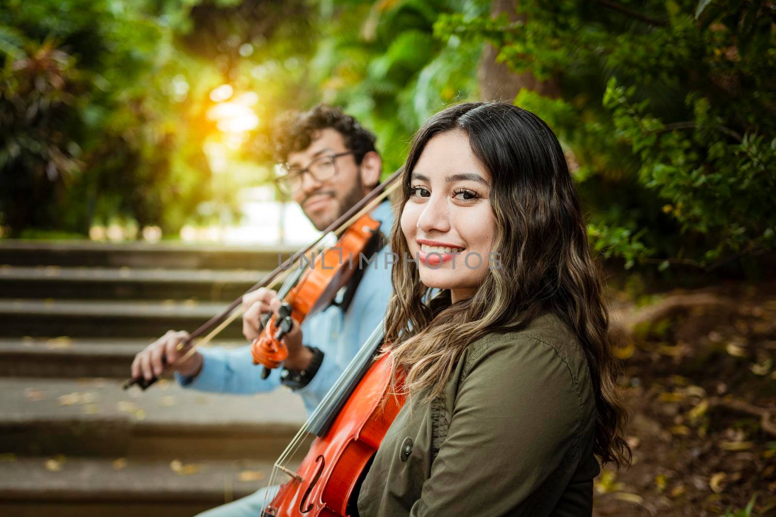 Portrait of two young violists sitting outside. Man and woman violinist sitting on the stairs. Two young violinists sitting outdoors looking at the camera. Concept of two young violinists by isaiphoto