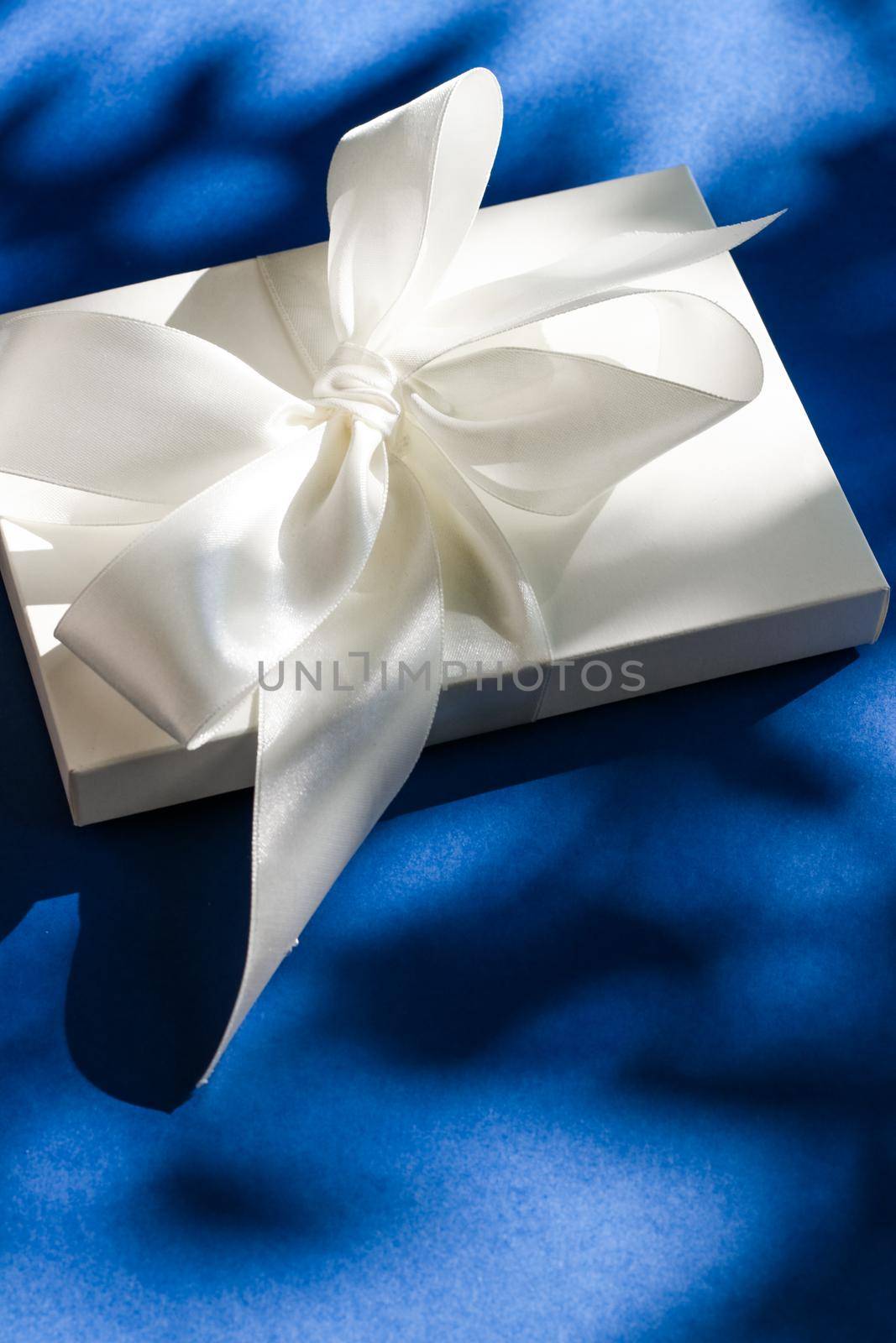 Anniversary celebration, shop sale promotion and bridal surprise concept - Luxury holiday white gift box with silk ribbon and bow on blue background, luxe wedding or birthday present