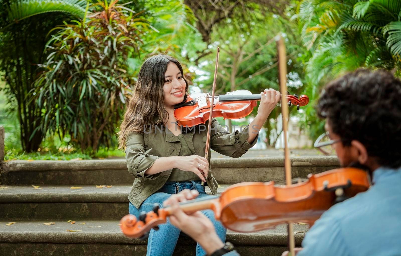 Portrait of violinist people sitting on stairs playing violin. Portrait of two young violists playing violin sitting on stairs outside. Man and woman sitting on the stairs playing a melody with violin by isaiphoto