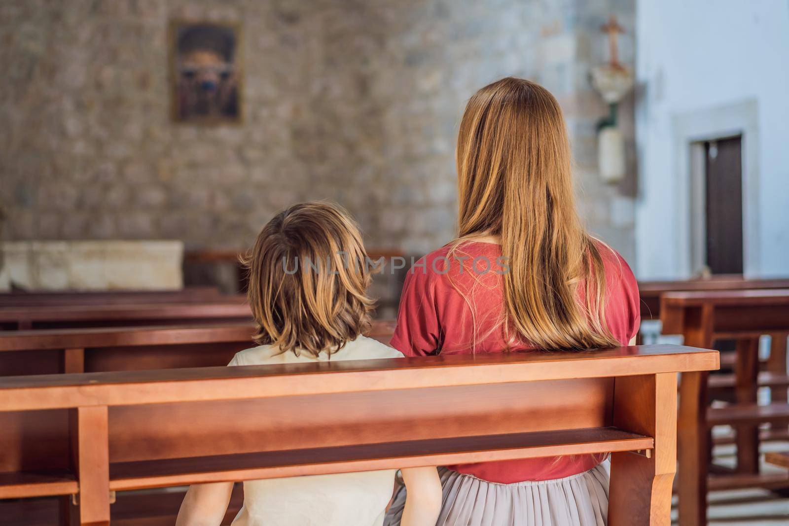 A Christian mom tells her son Bible stories about Jesus sitting in church. Faith, religious education, modern church, mother's day, maternal responsibilities, mother's influence on son's worldview formation.