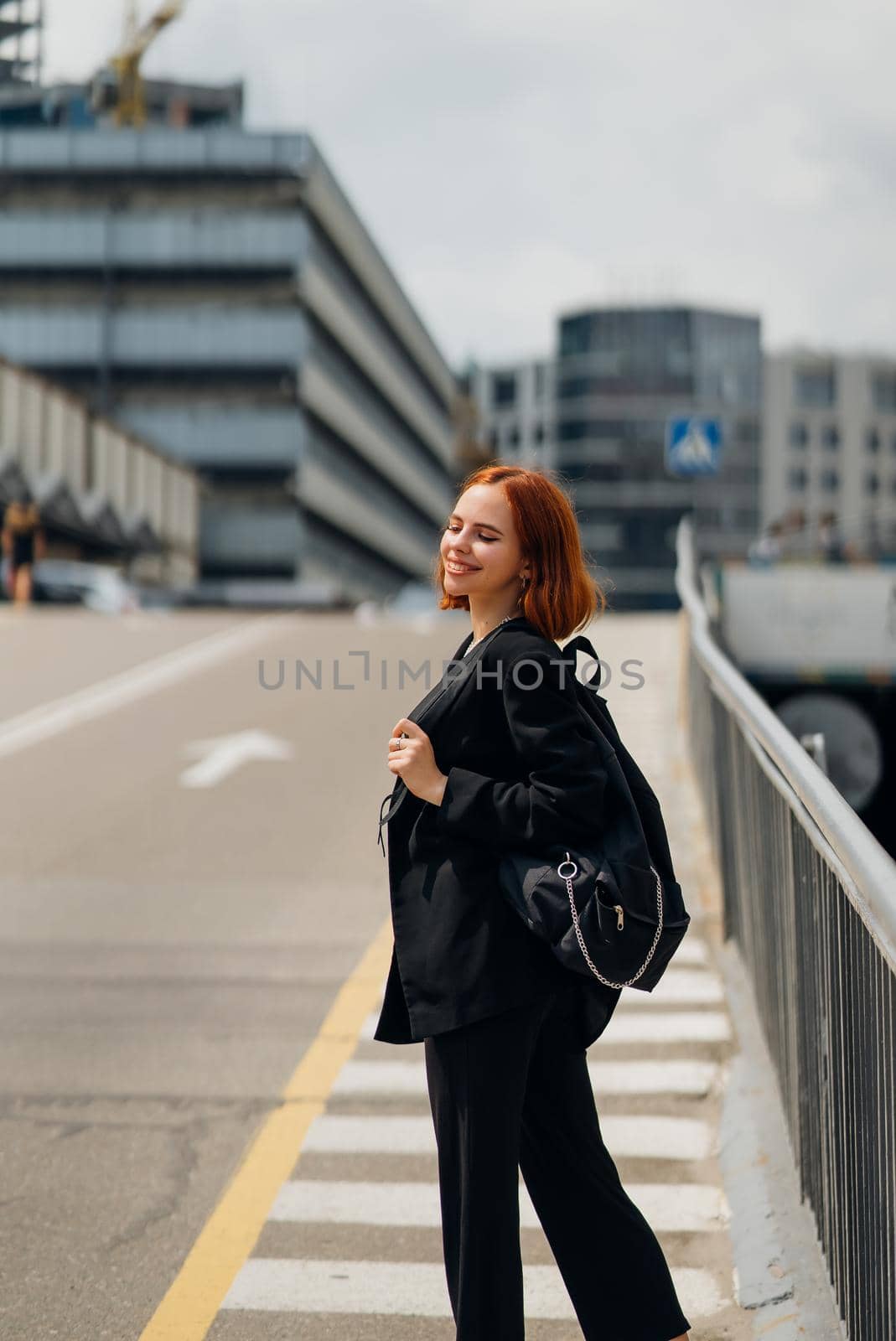 Young beautiful smiling happy woman with backpack poses on a camera while standing on the road