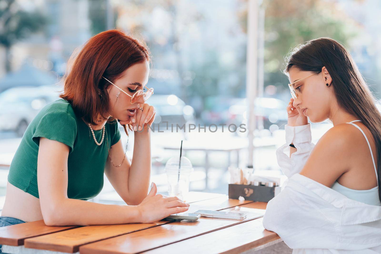 Two pretty girlfriends talking while sitting in a bar at the city street