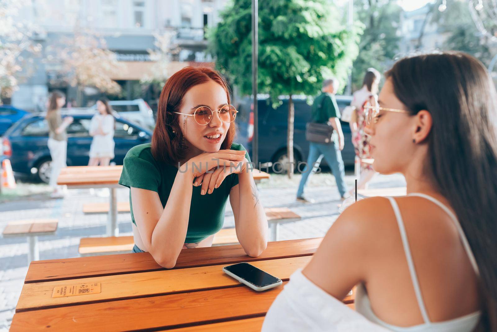 Two pretty girlfriends talking while sitting in a bar at the city street