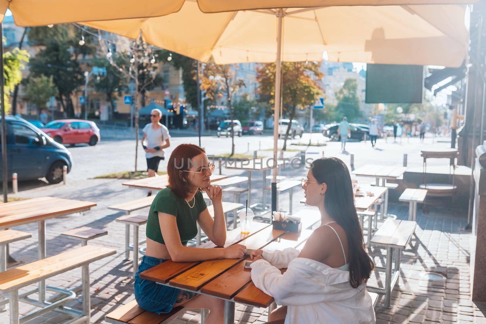 Two pretty girlfriends talking while sitting in a bar at the city street