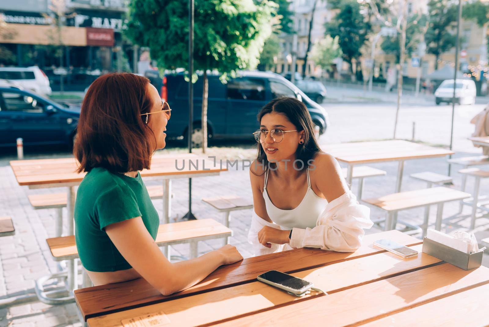 Two pretty girlfriends talking while sitting in a bar at the city street