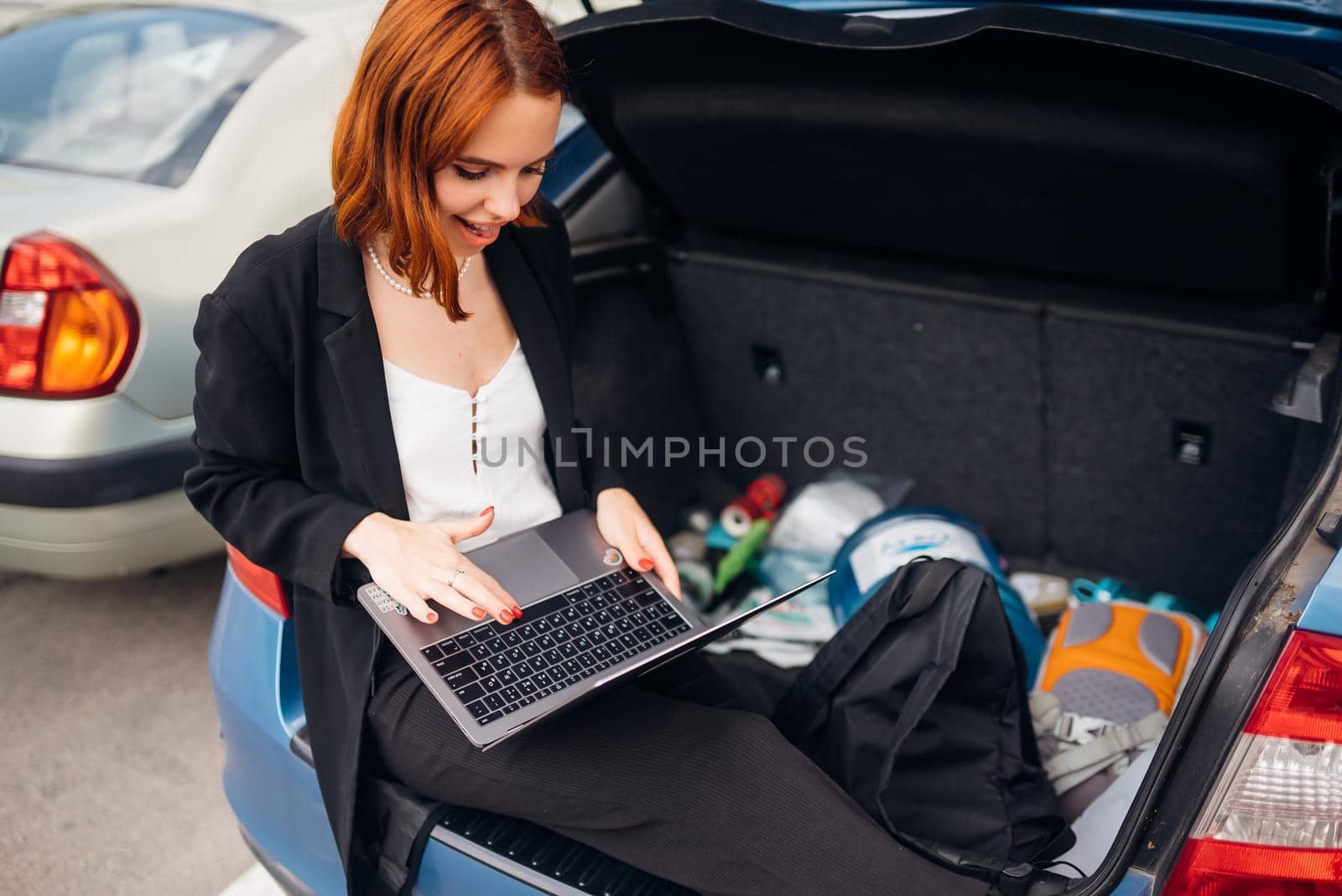 Business attractive young woman working on laptop while sitting in trunk of car while traveling