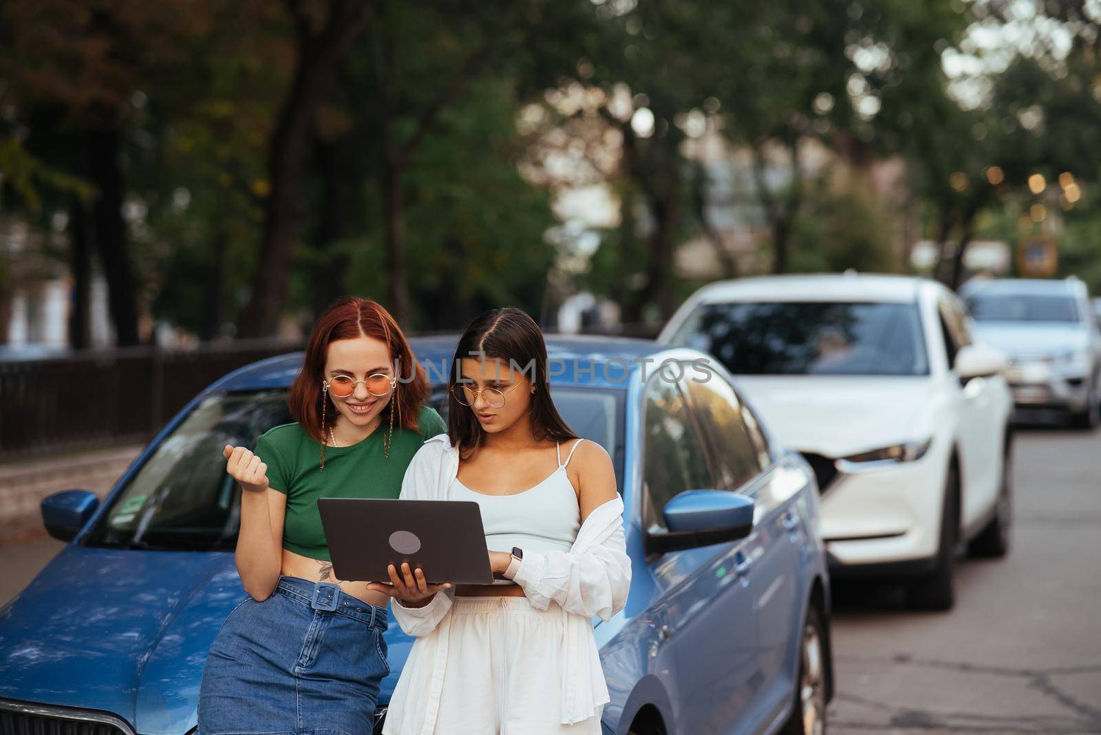 Two young women with a laptop near the car on the road