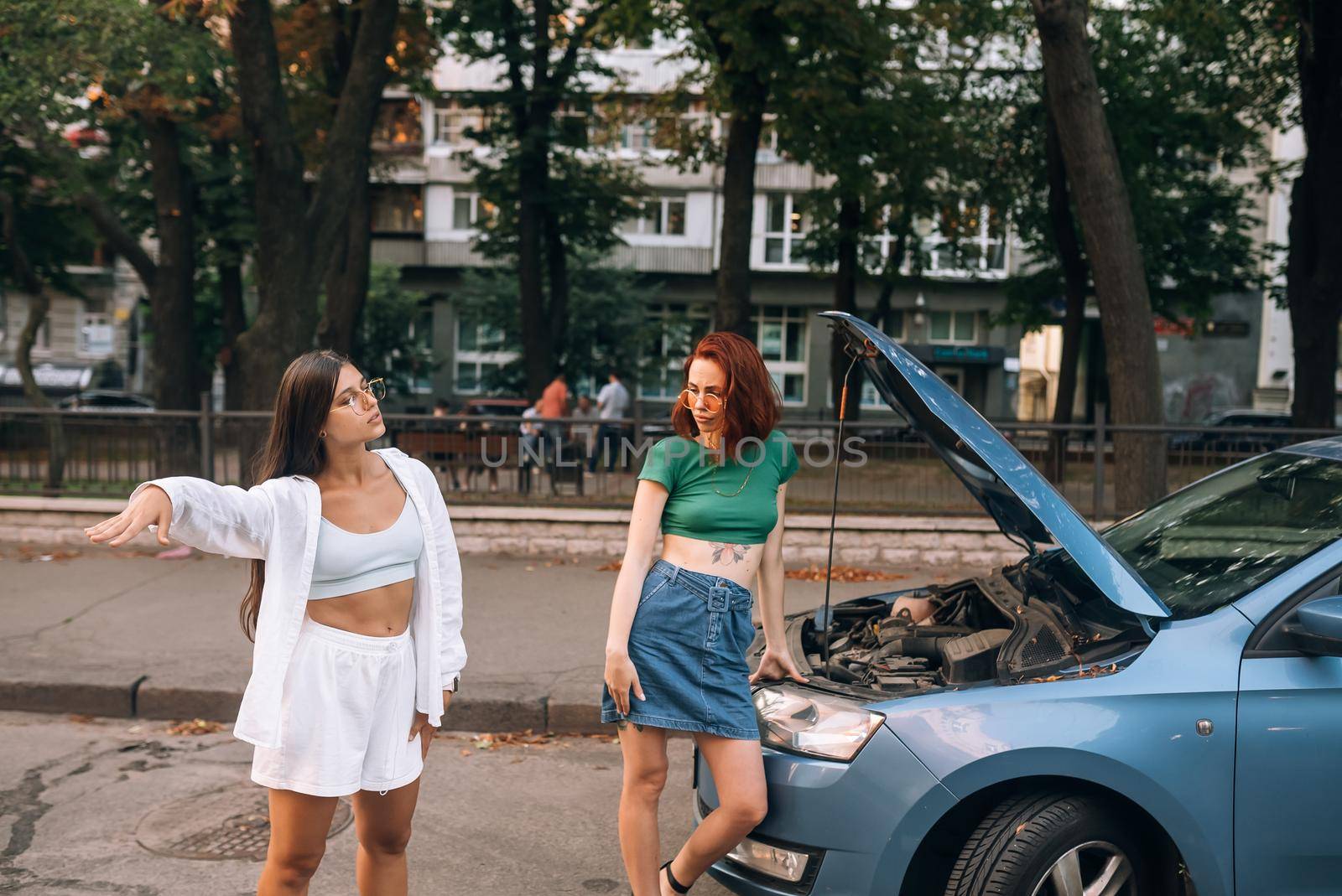 Two women with broken car road look for help. by teksomolika