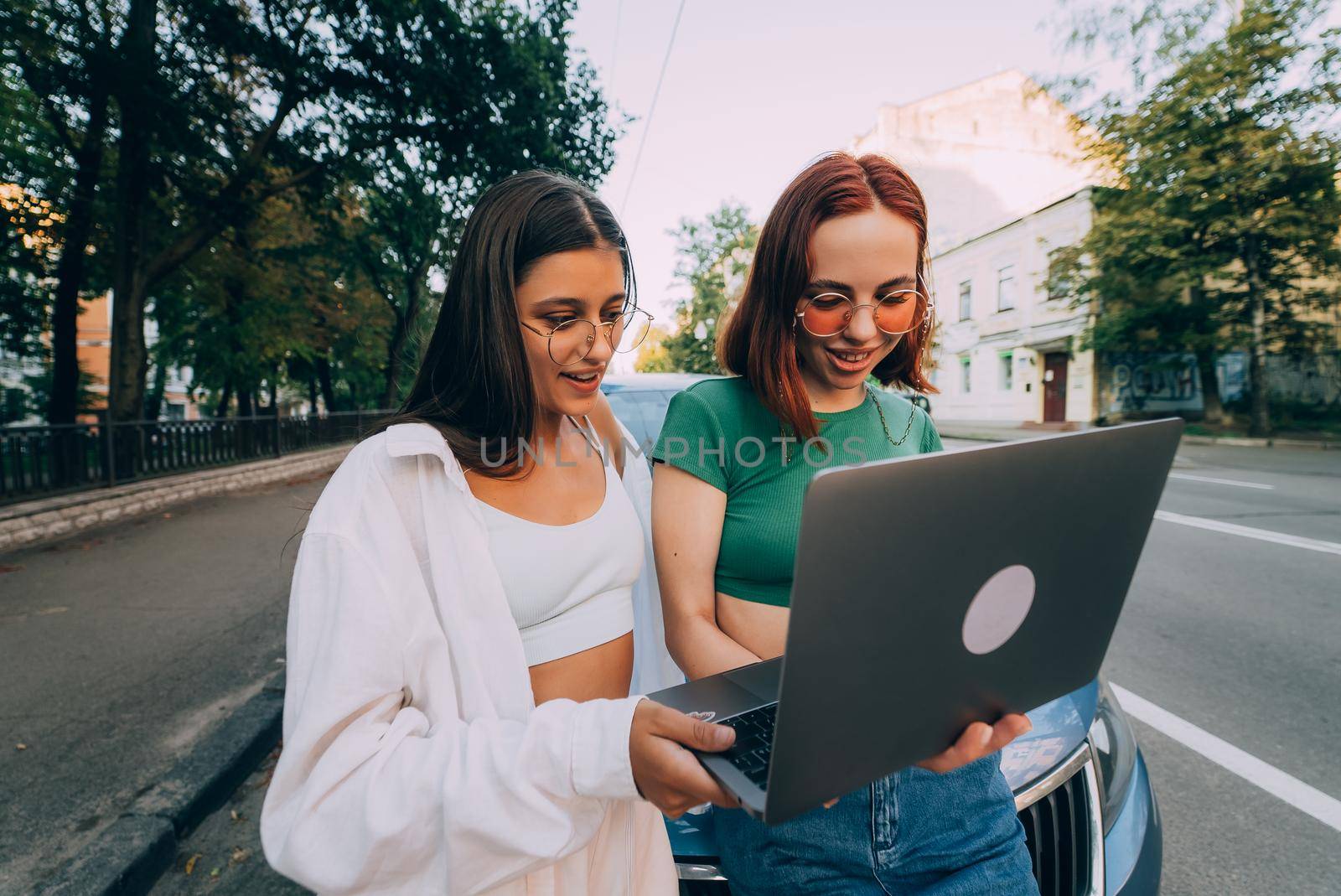 Two young women with a laptop near the car on the road