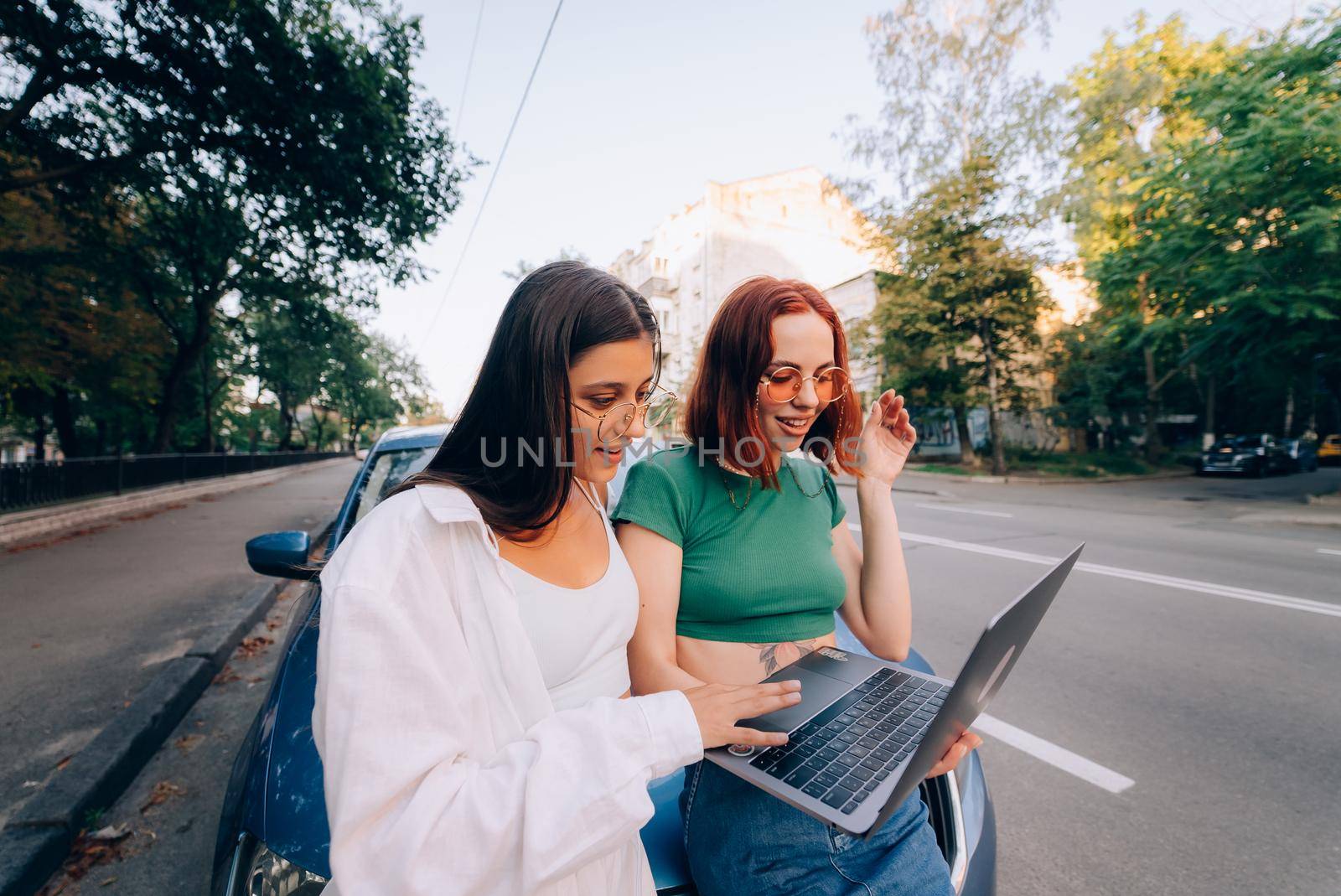 Two young women with a laptop near the car on the road