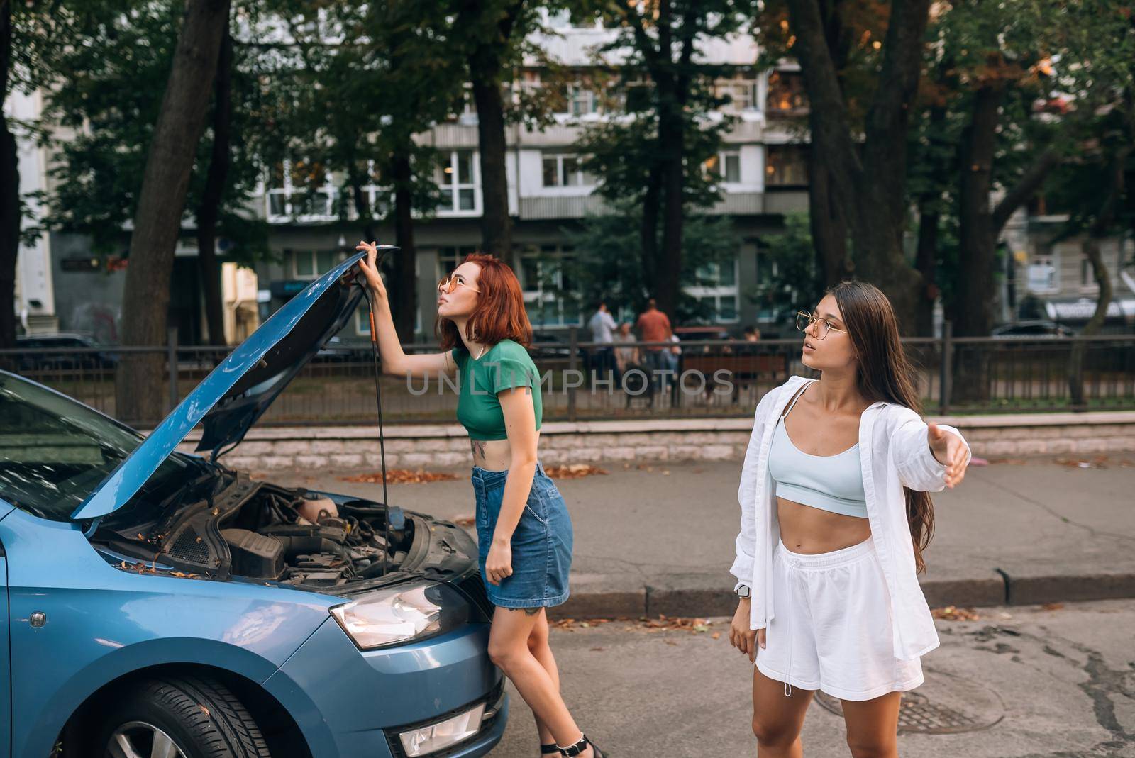 Two women with broken down car on the road look for someone help.