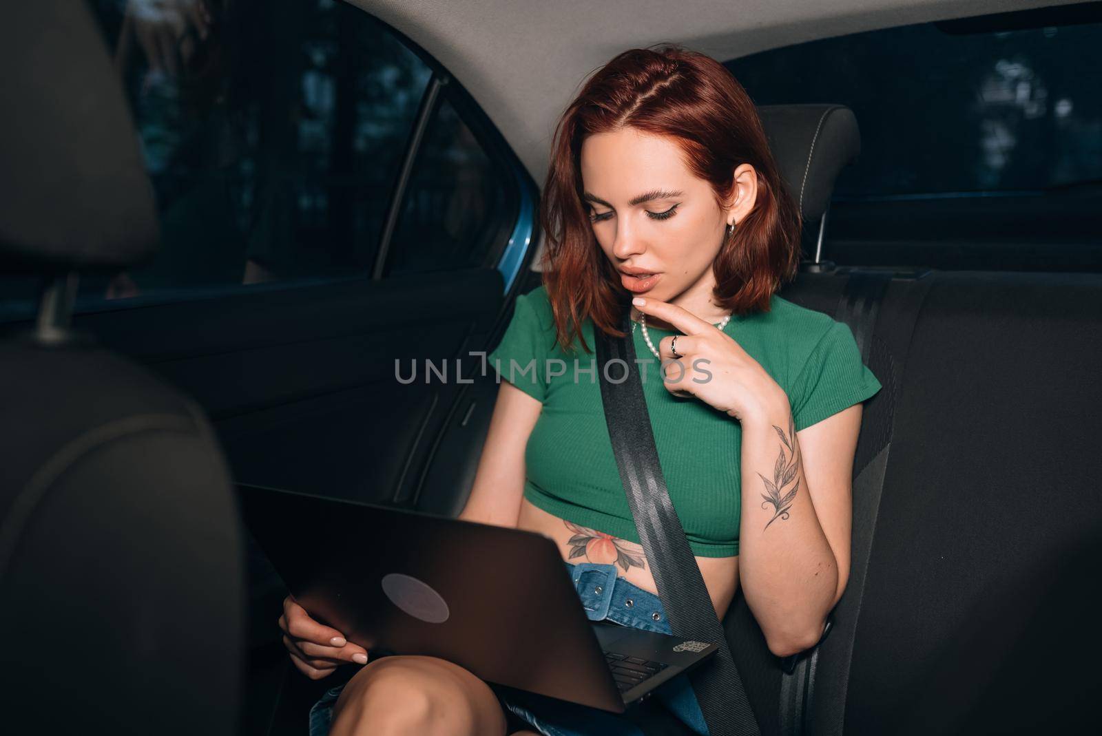 Beautiful woman is using a laptop and smiling while sitting on back seat in the car
