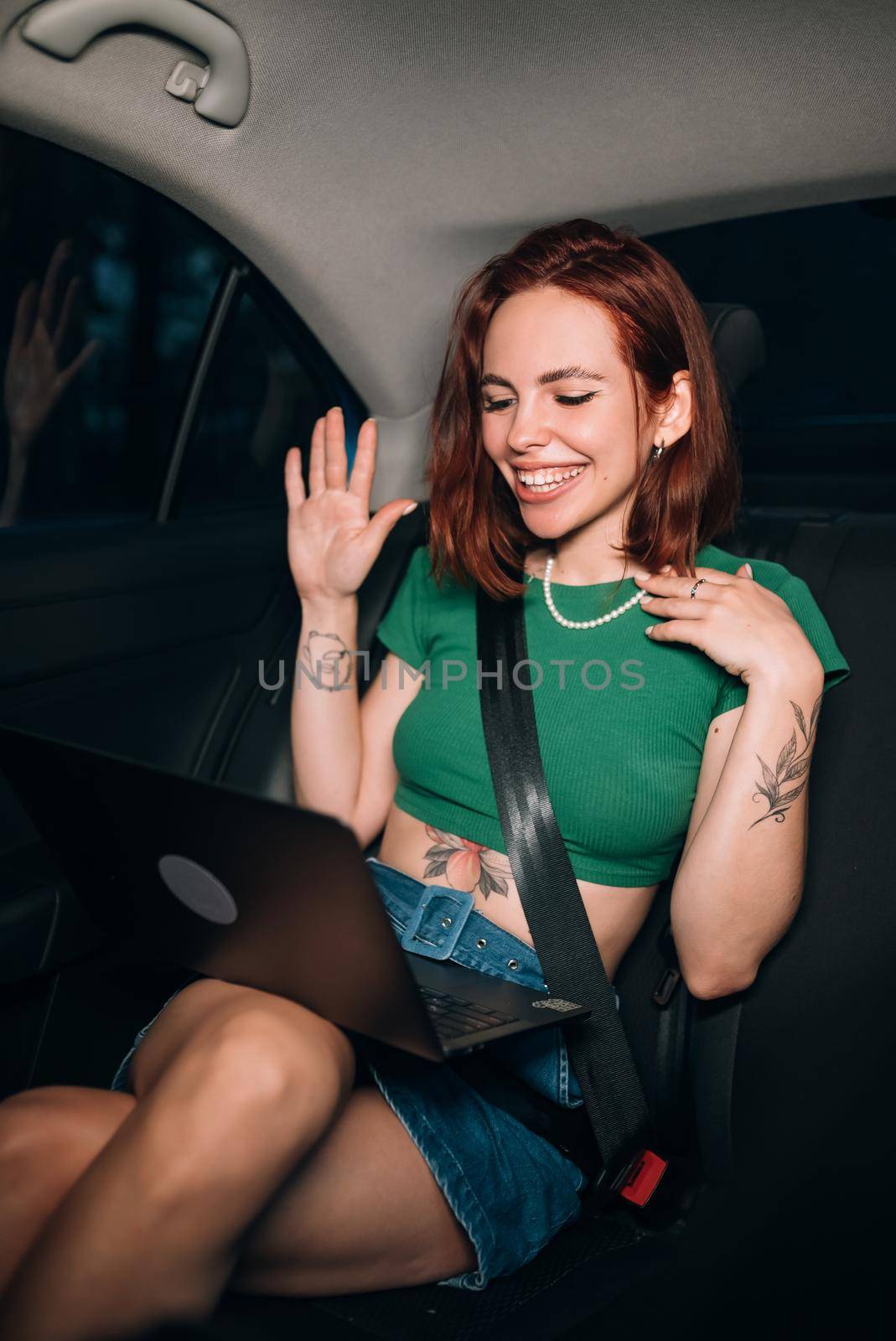 Beautiful woman is using a laptop and smiling while sitting on back seat in the car