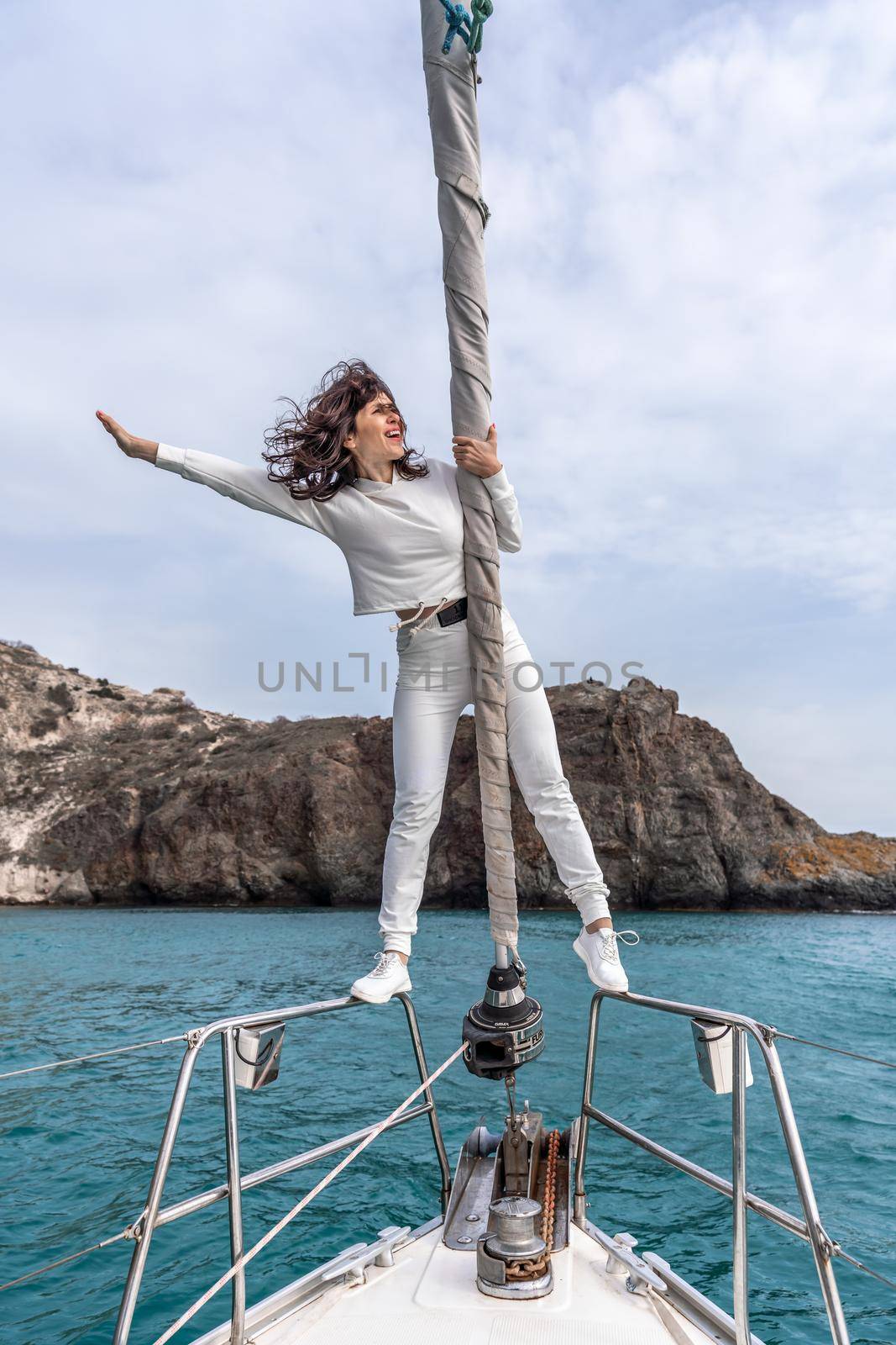 Woman standing on the nose of the yacht at a sunny summer day, breeze developing hair, beautiful sea on background.