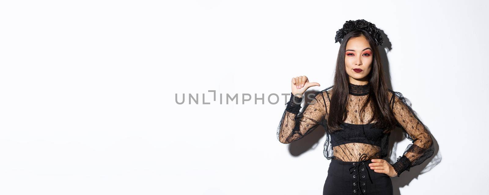 Confident stylish asian woman looking determined, wearing black lace dress for halloween party, pointing at herself sassy, standing over white background by Benzoix