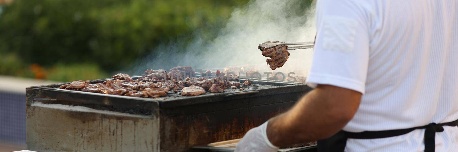 Close-up of metal construction for frying meat in nature, male chef do grill. Picnic on fresh air, frying meat and vegetable. Street food, barbeque concept