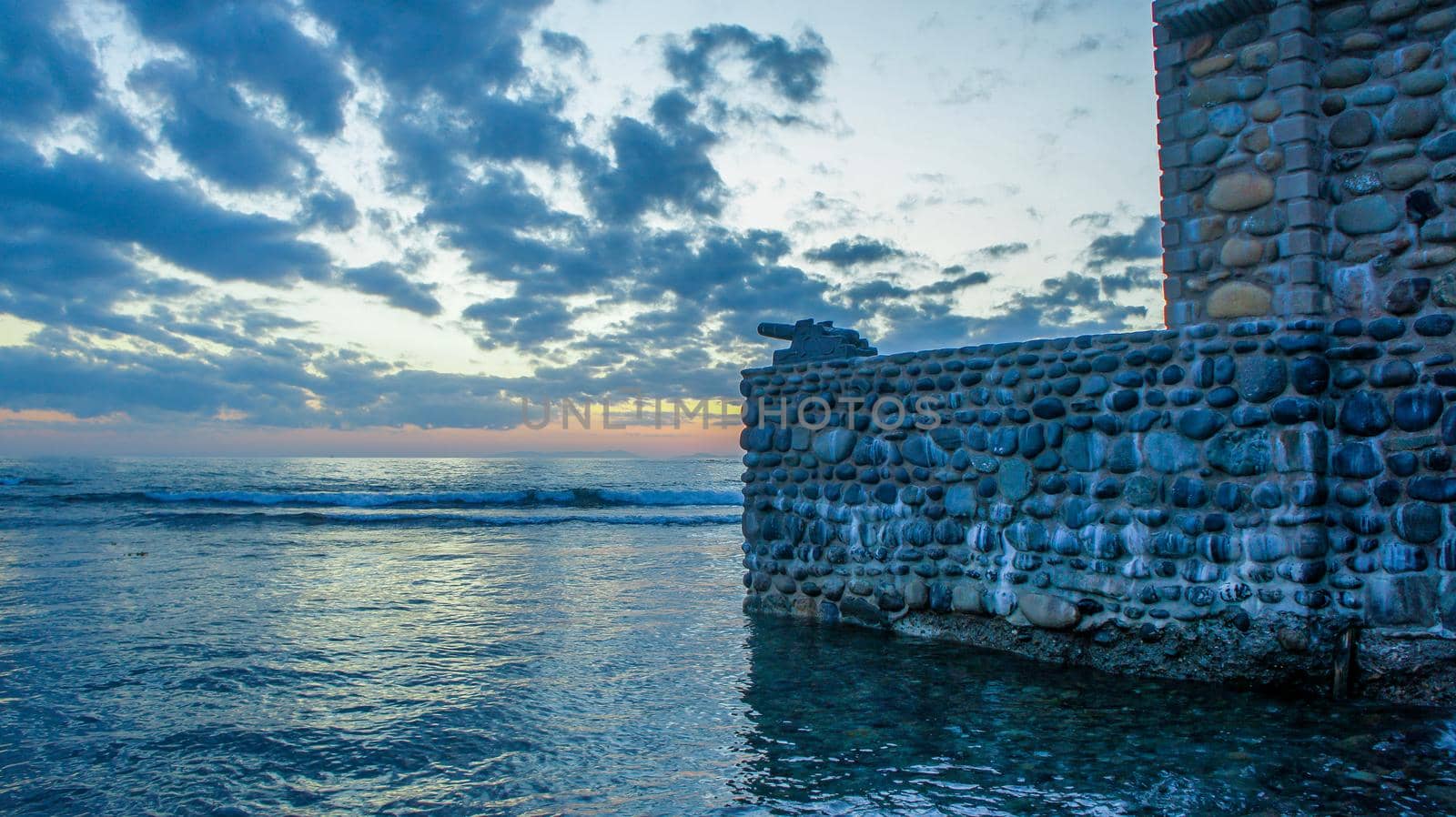 Stone wall with a gun on the background of the sea landscape. by Vvicca