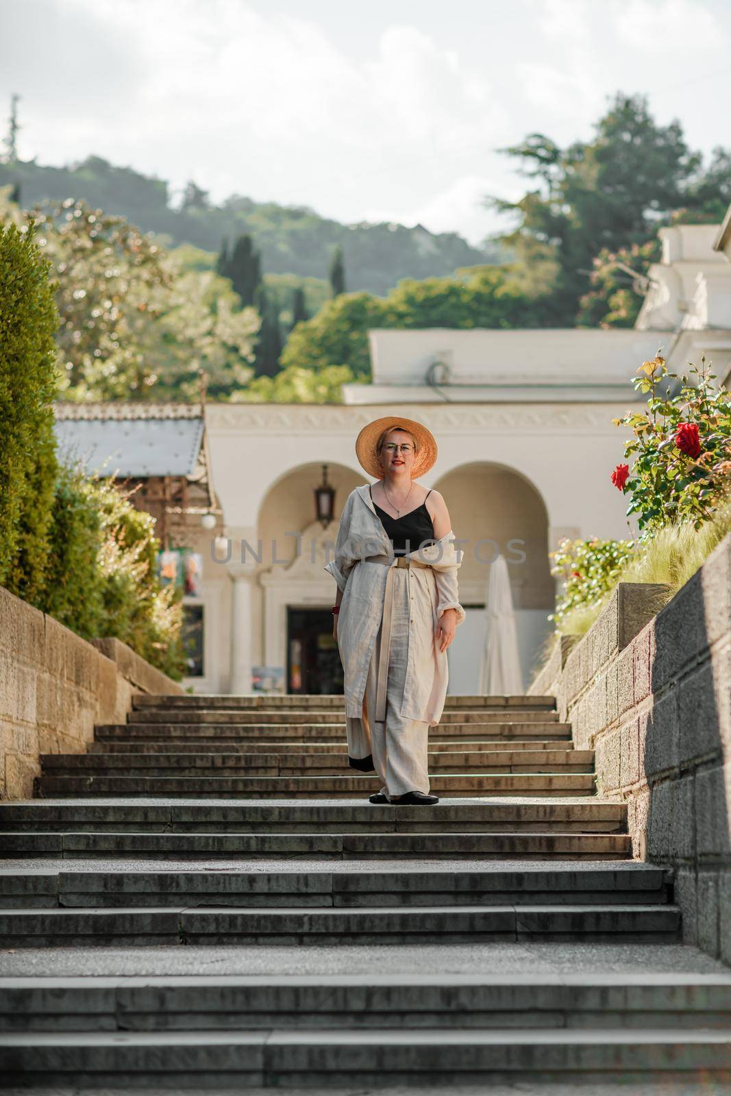 Woman on the stairs in the park. A middle-aged lady in a hat in a white outfit with a bag walks around the Livadia Palace.