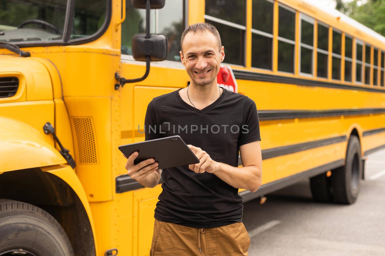 handsome teacher looking at camera school bus blurred on background.